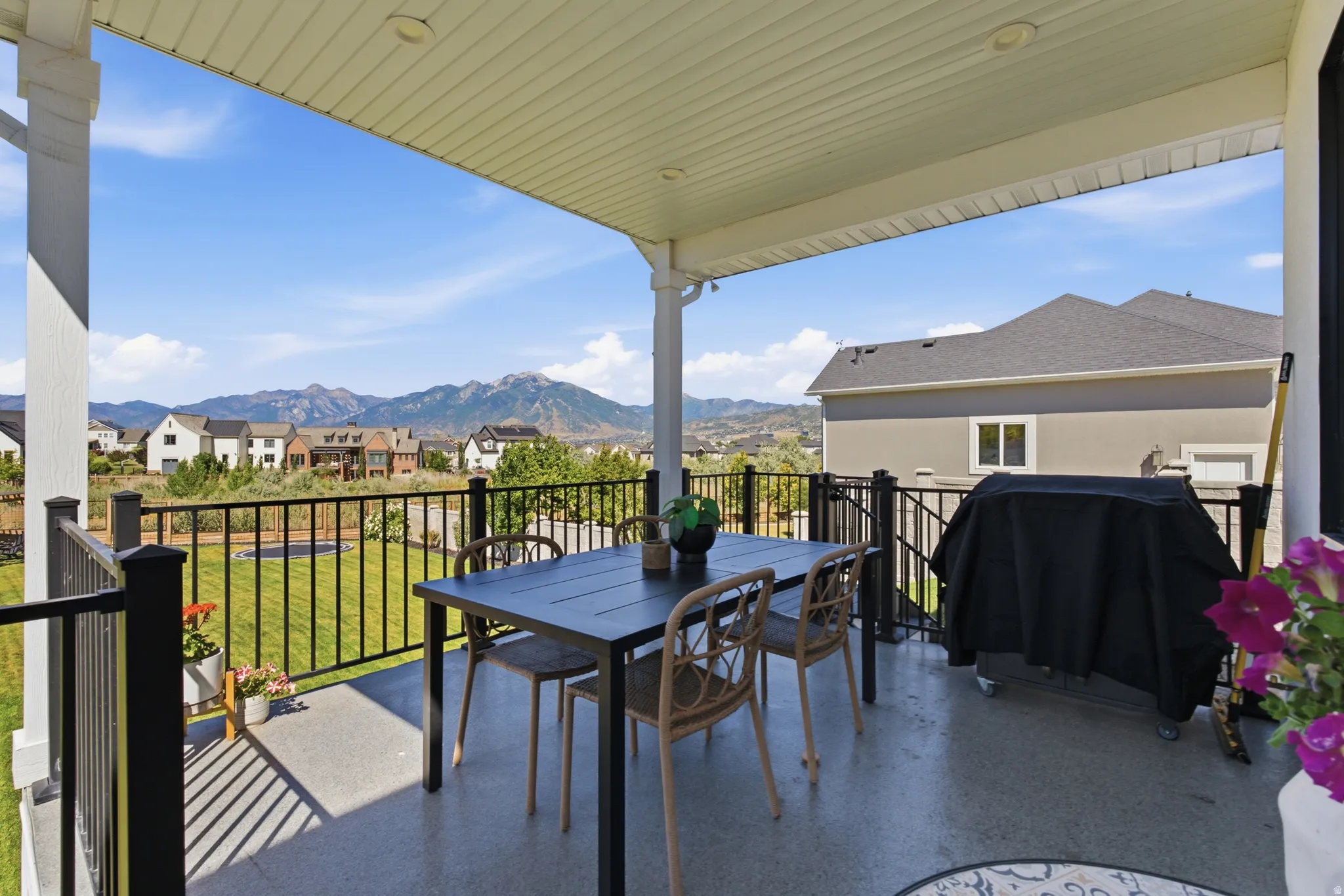Covered outdoor patio with a concrete surface, featuring a black metal railing and white support columns