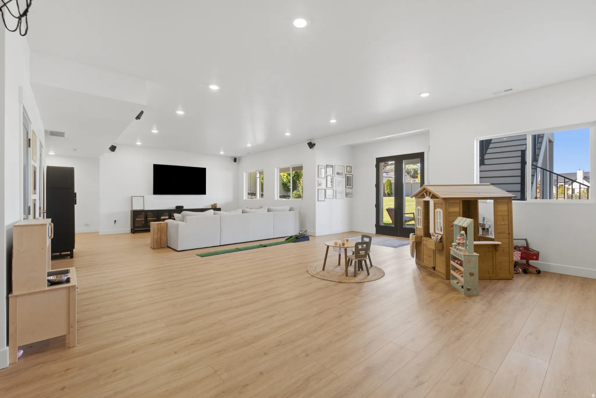Spacious lower-level living area featuring light wood-finish flooring, recessed lighting, and white walls