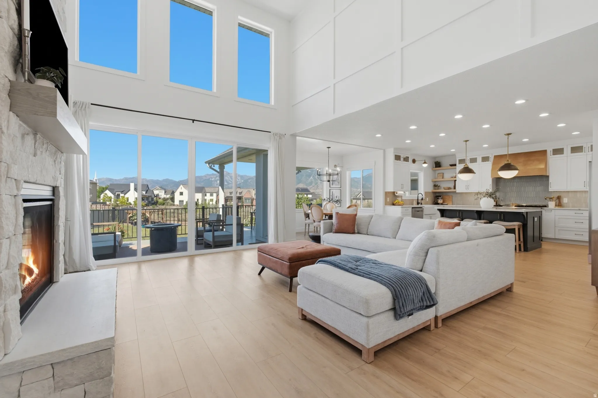 Open-concept living area featuring a stone-clad fireplace with a light-colored mantel, light wood-finish flooring, and large sliding glass doors opening to an outdoor patio space
