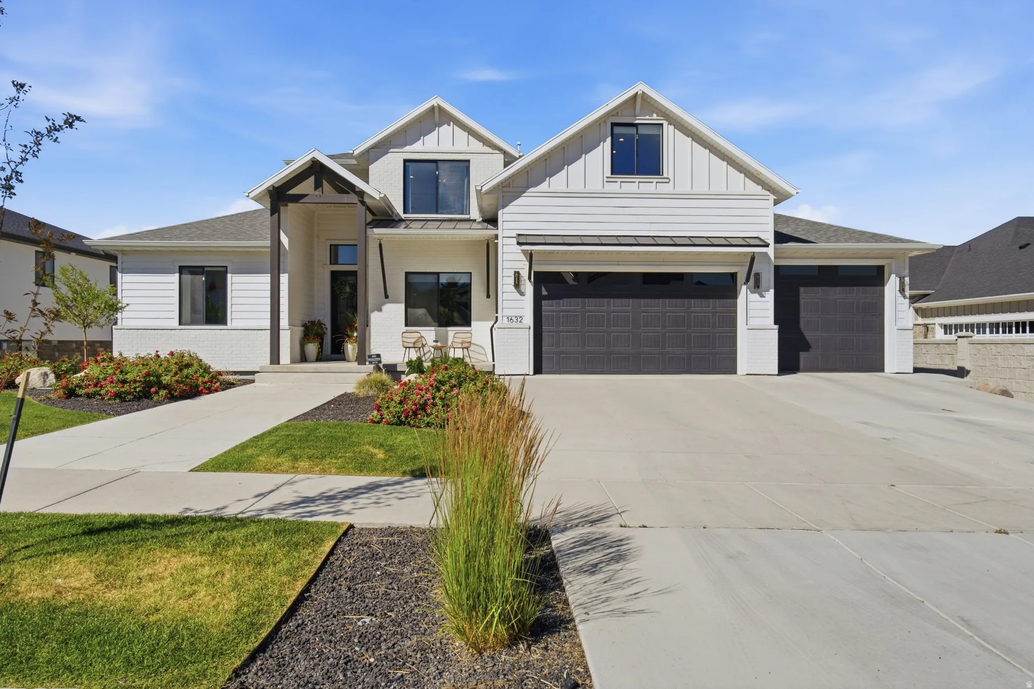 Modern farmhouse exterior featuring white siding, dark trim windows, a covered entry with exposed beam accents, and an attached two-car garage with dark paneled doors