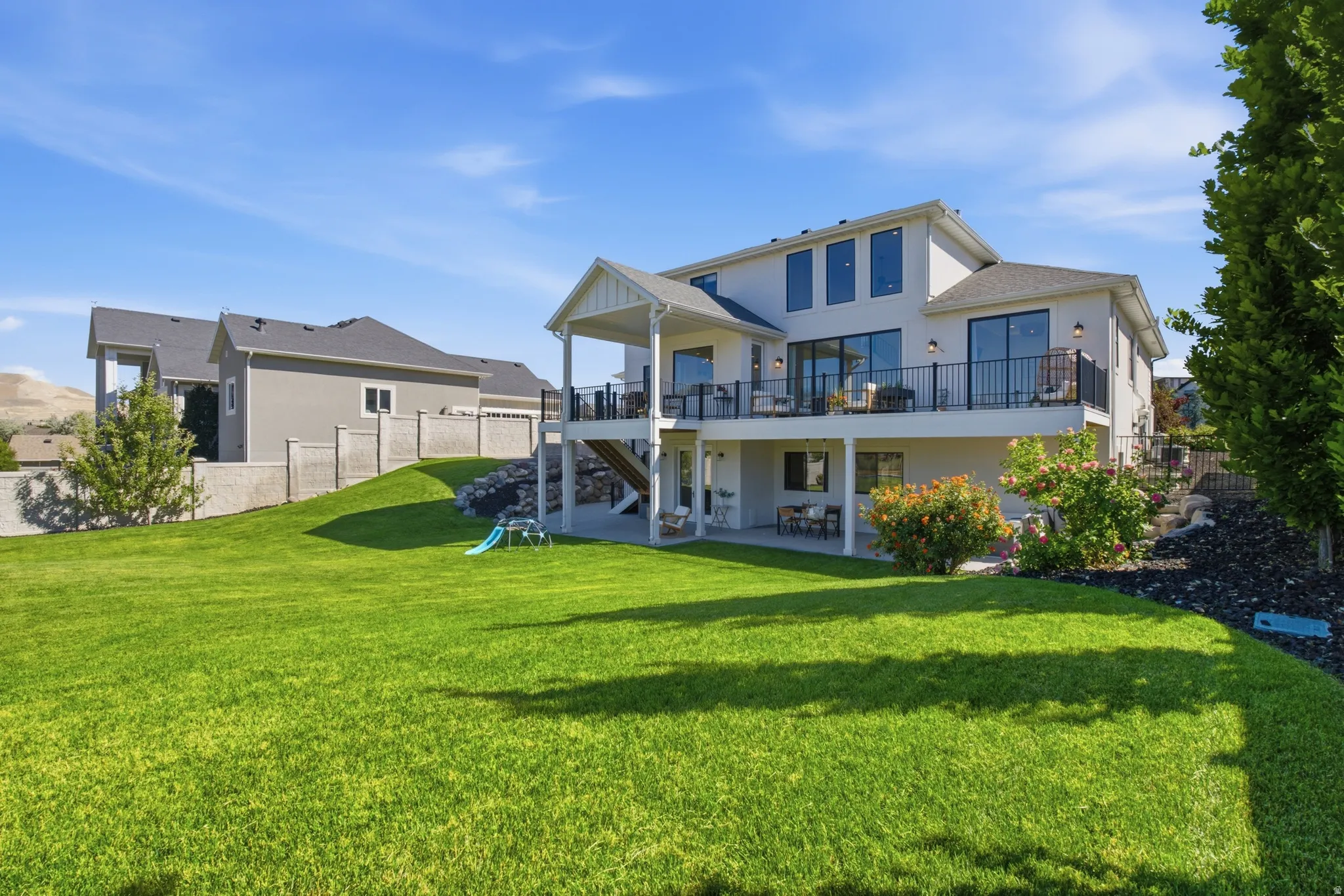 Expansive rear exterior featuring a raised deck with black metal railings, a covered patio, and a large manicured lawn