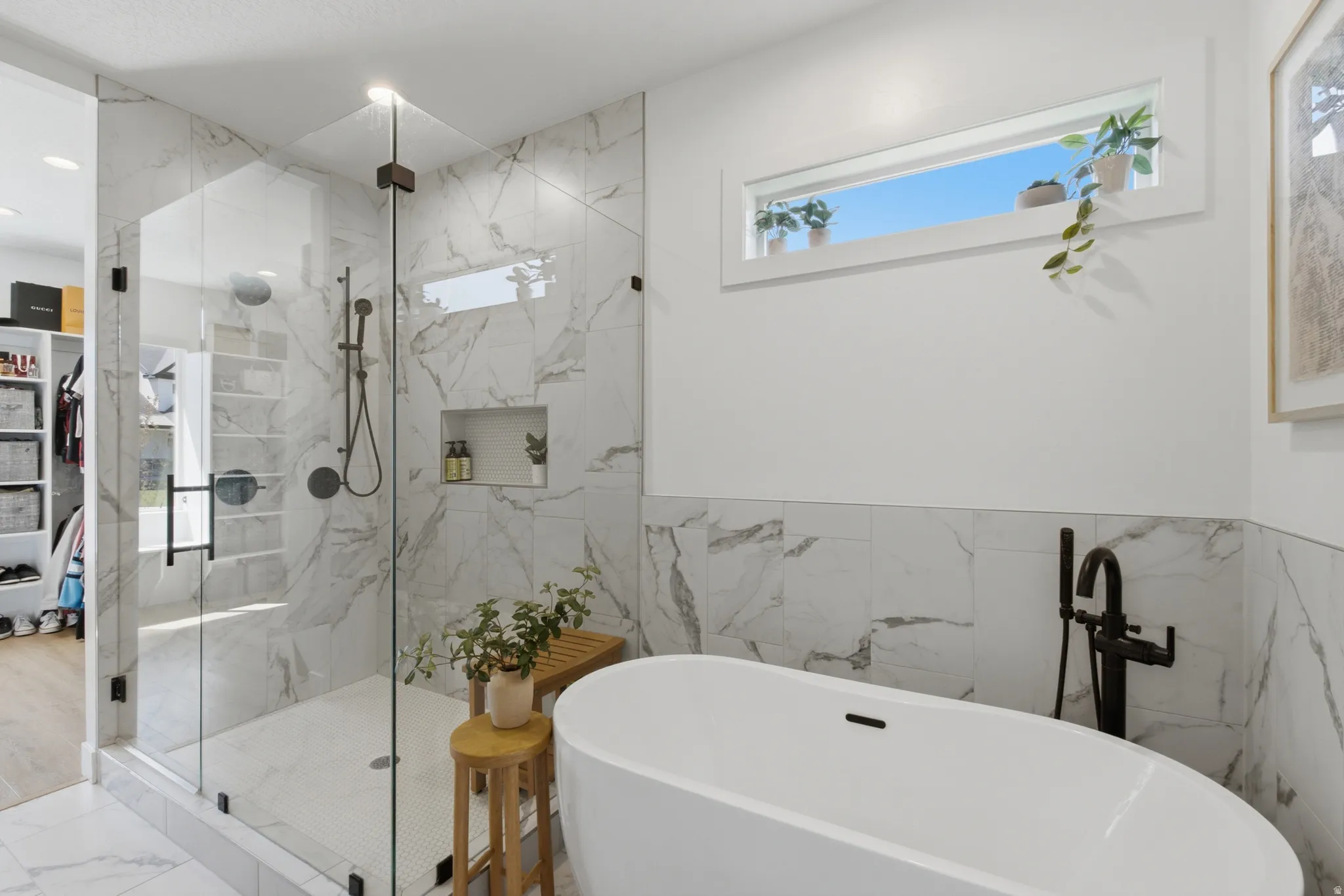 Contemporary bathroom featuring a freestanding soaking tub with a matte black floor-mounted faucet, a spacious glass-enclosed shower with marble-finish tile, and a built-in shower niche