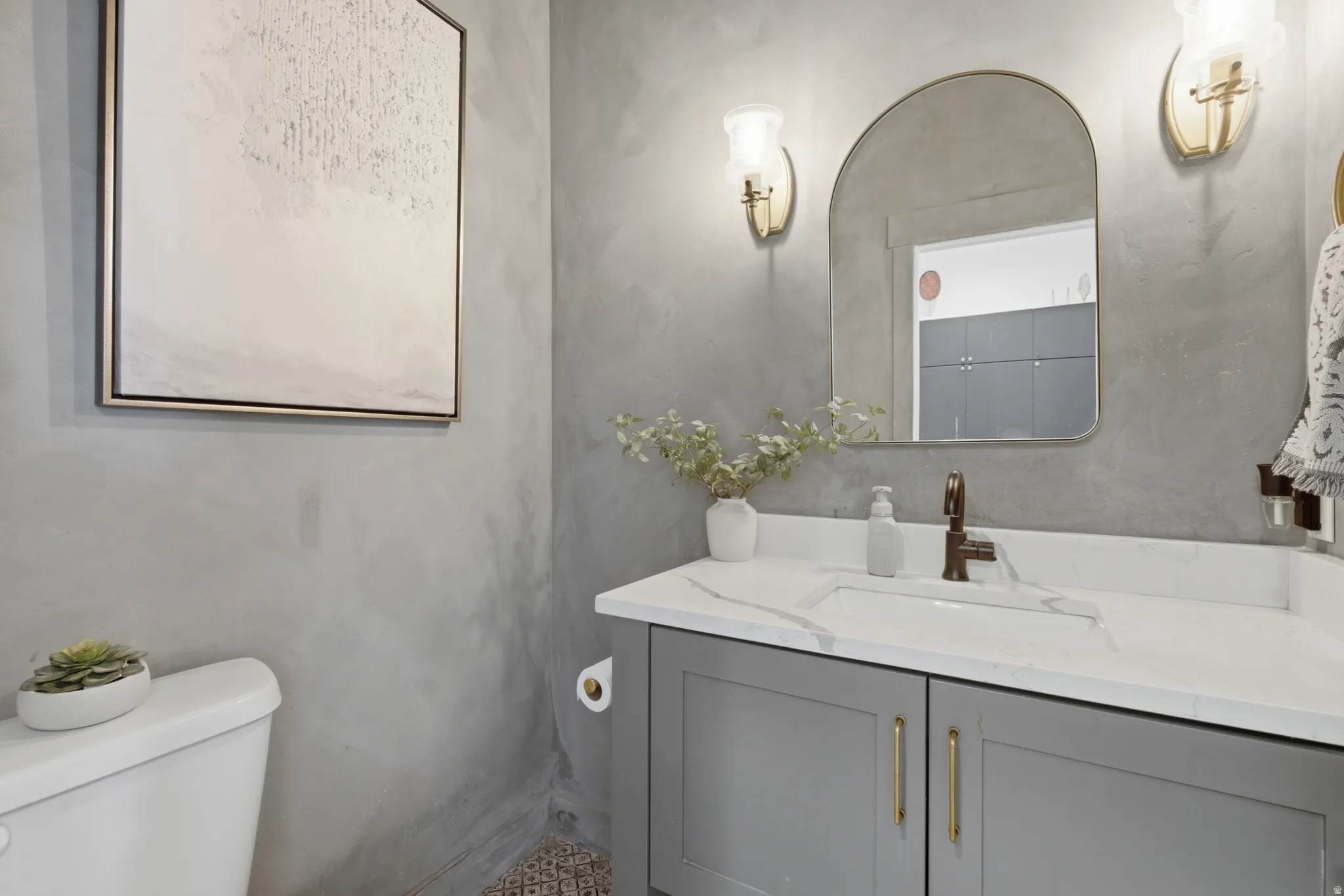 Powder room featuring a gray vanity with a white countertop and integrated sink, a curved mirror, and brass-toned wall sconces