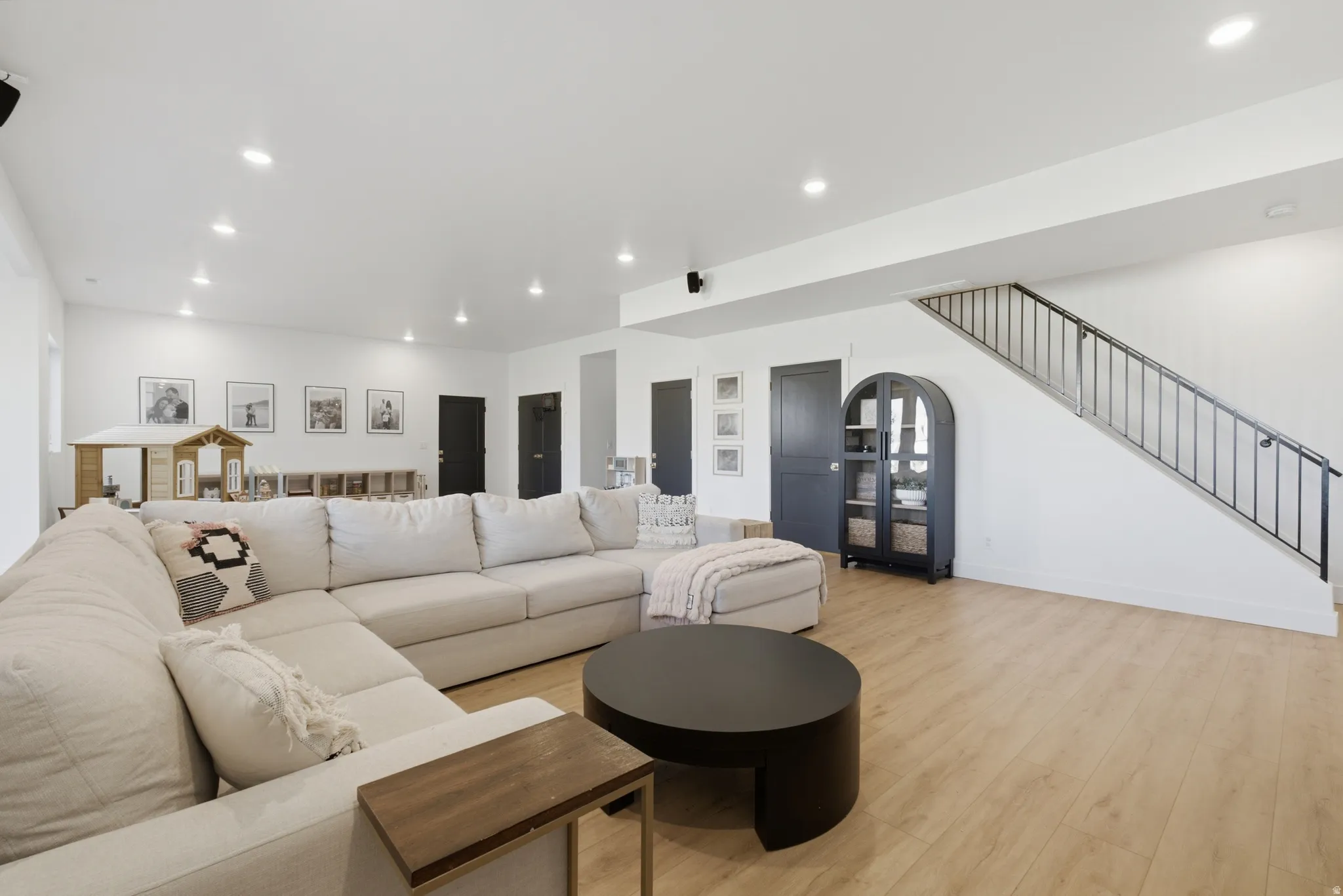 Spacious room featuring light wood-finish flooring, recessed lighting, and a staircase with a black metal railing
