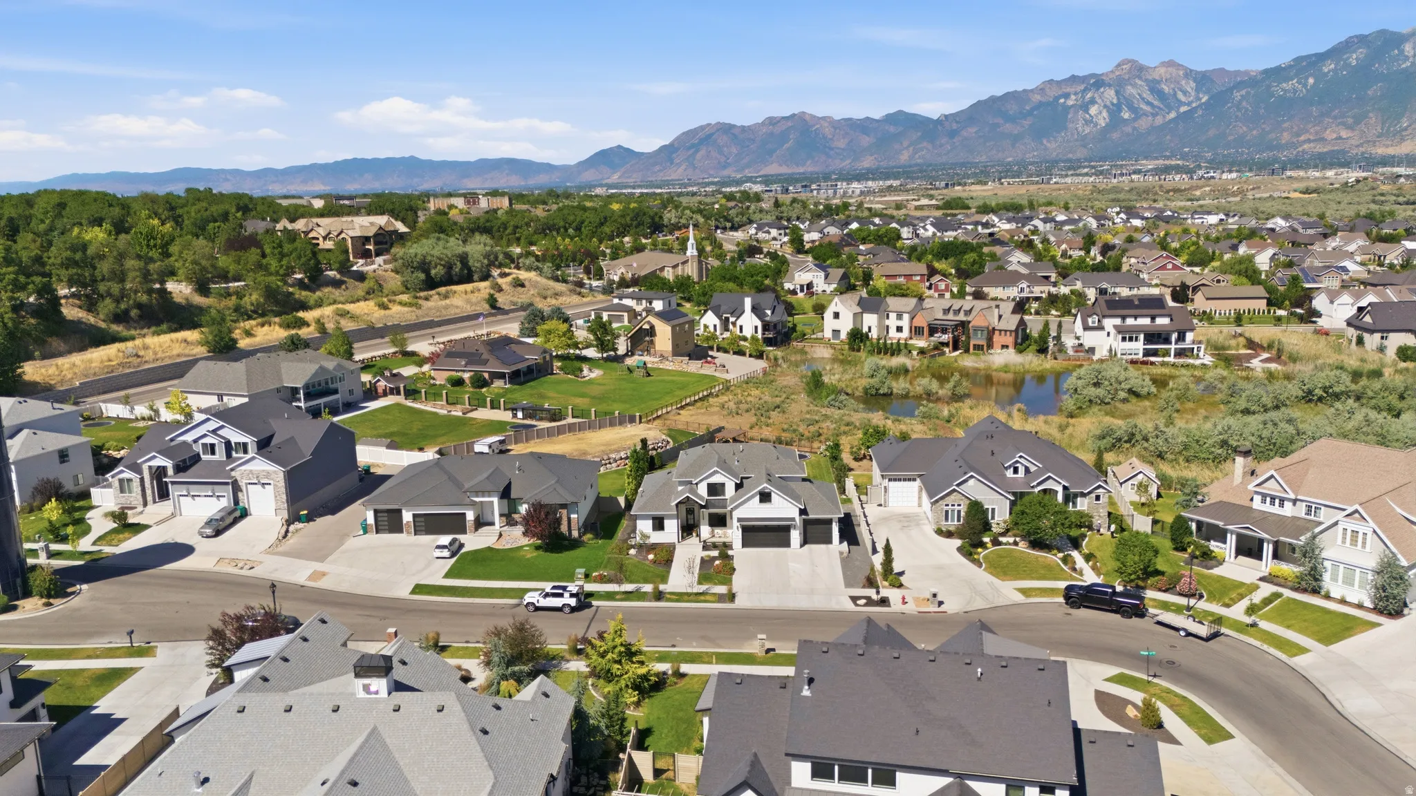 Residential neighborhood featuring mature landscaping, diverse architectural styles, paved streets, and mountainous terrain in the distance