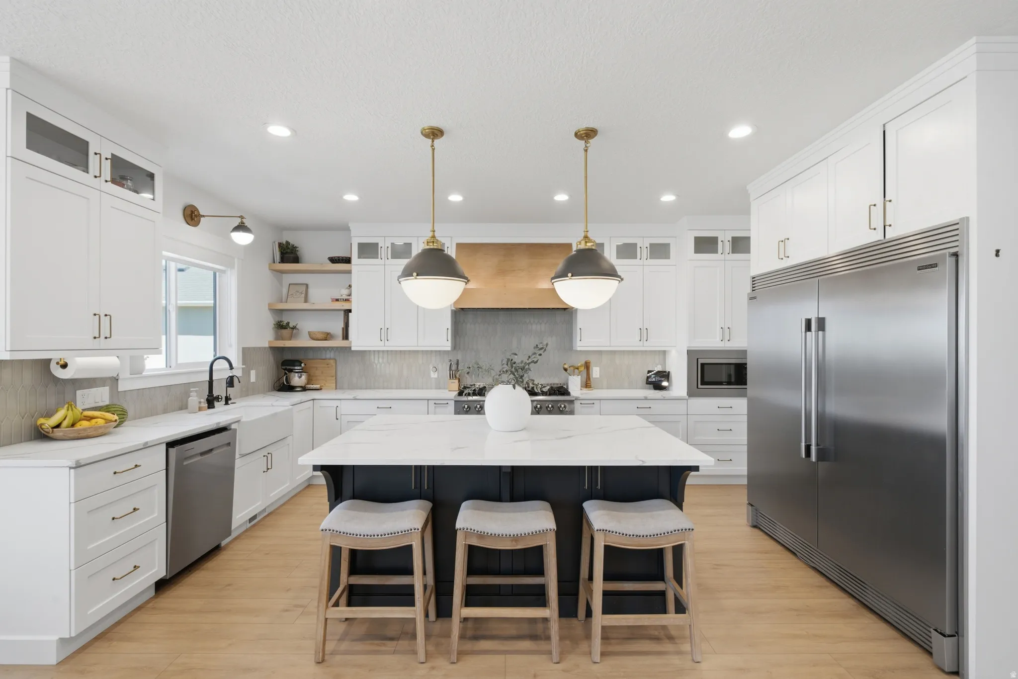 Gourmet kitchen featuring a large central island with seating, white shaker cabinetry, stainless steel appliances, and wood-finish flooring