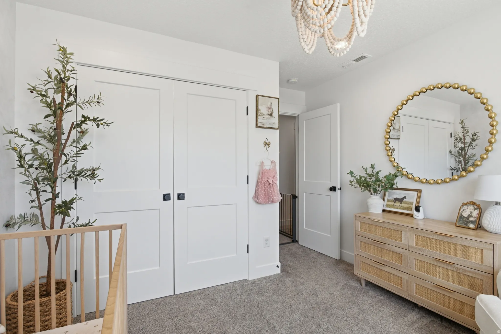 White shaker-style bi-fold closet doors featuring matte black hardware, gray carpet flooring, and a beaded chandelier