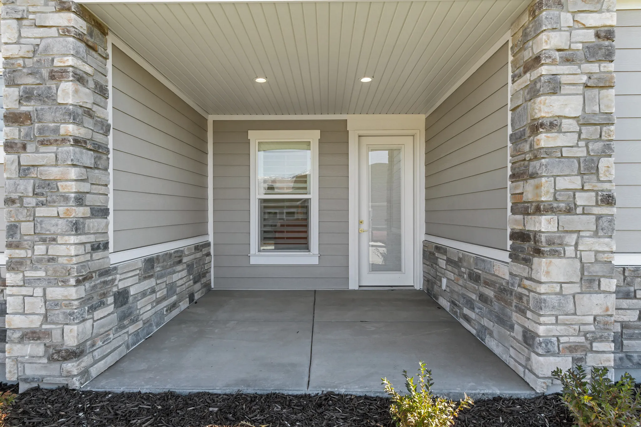Covered front porch featuring stacked stone columns and wainscoting, horizontal siding, and a concrete slab