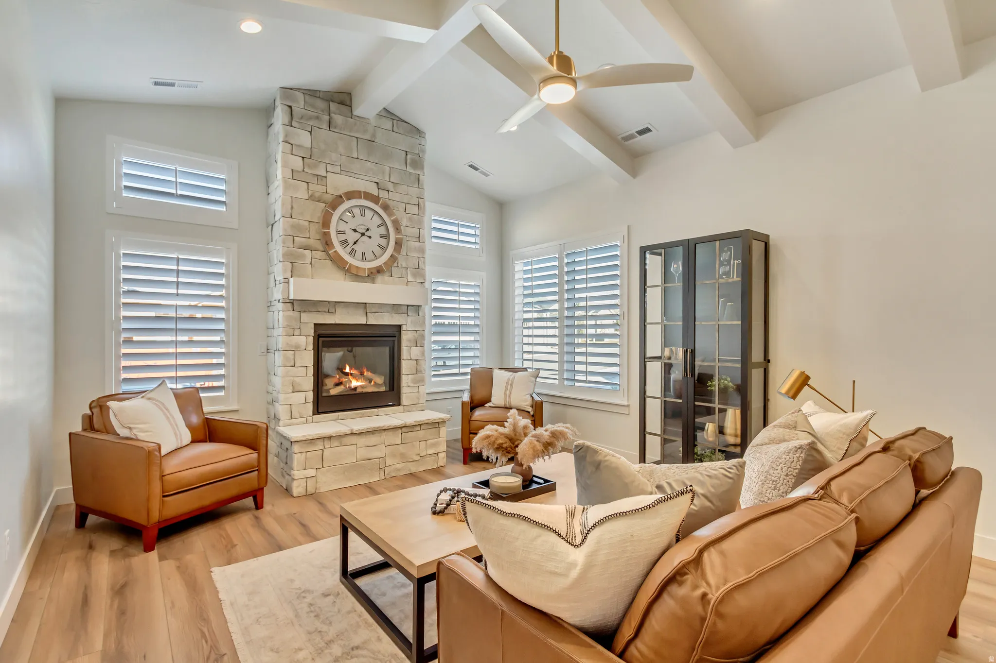 Living area featuring a stone-clad fireplace with a hearth, vaulted ceilings with exposed beams, and a ceiling fan with integrated lighting