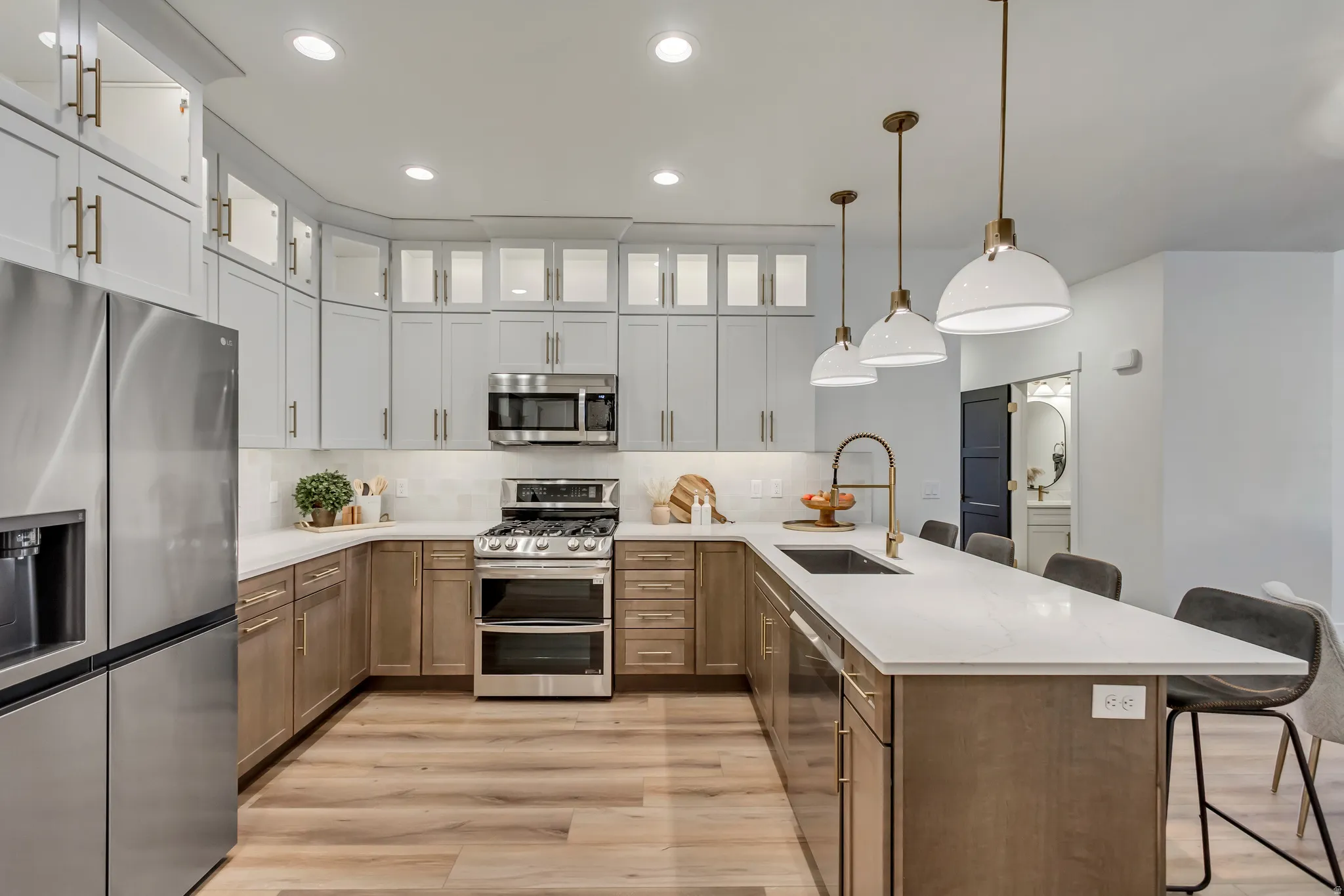Gourmet kitchen featuring a large island with sink, stainless steel appliances, two-tone cabinetry, wood-finish flooring, and recessed and pendant lighting