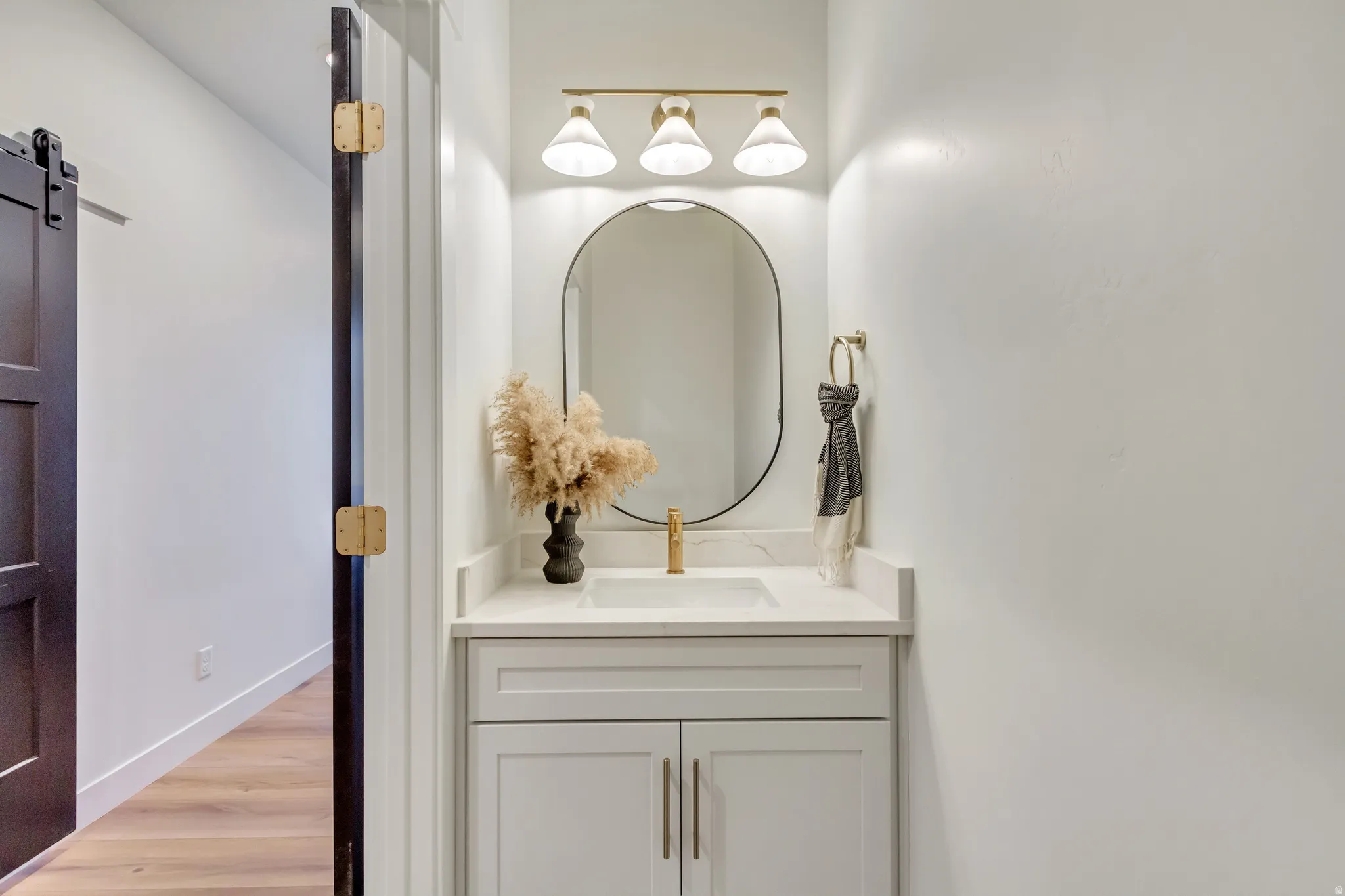 Bathroom vanity featuring a white countertop with an integrated sink, light-colored cabinetry with gold-tone hardware, and an oval mirror