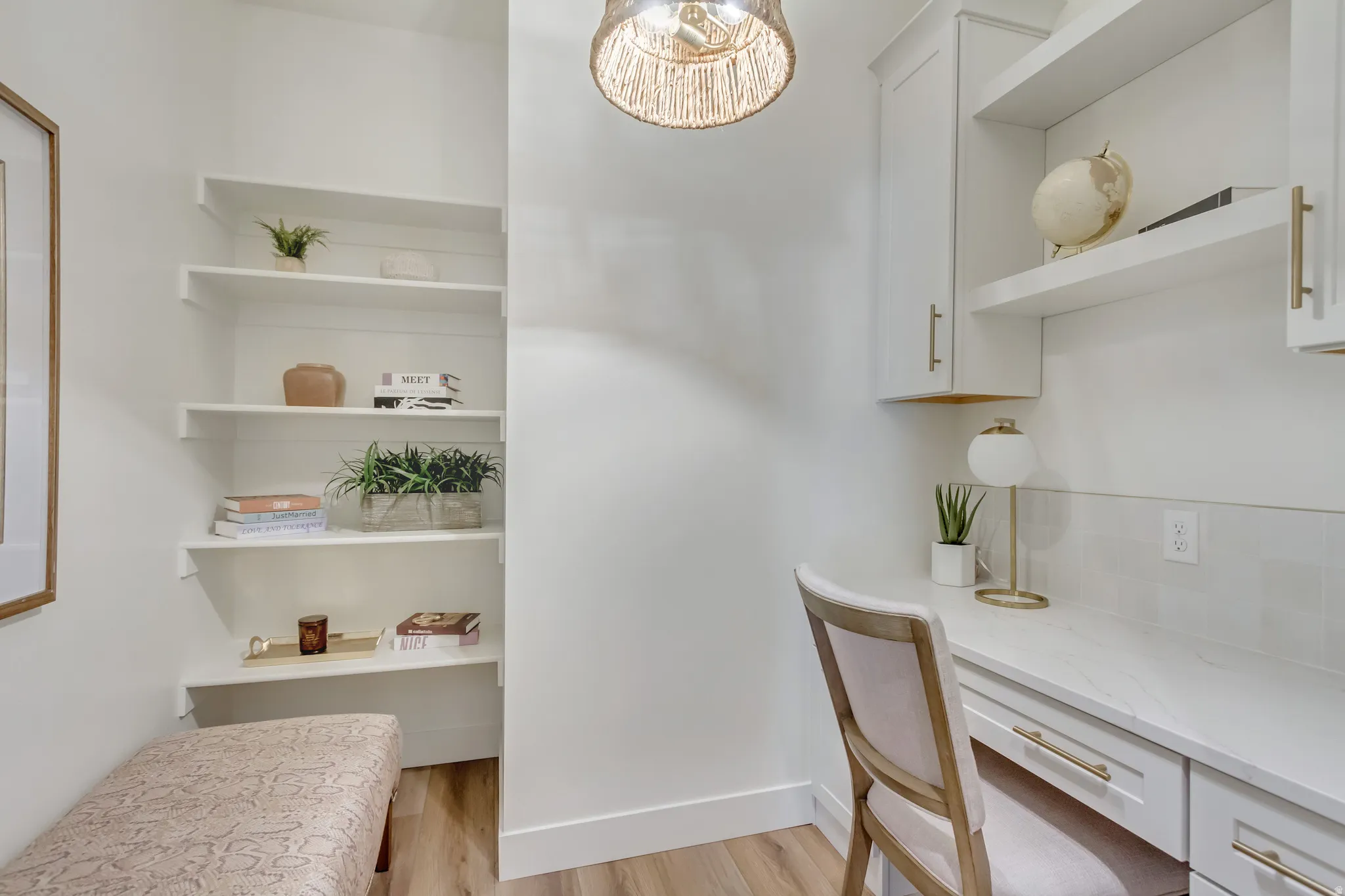 Integrated desk area featuring a built-in countertop, white cabinetry with gold-tone hardware, and open shelving