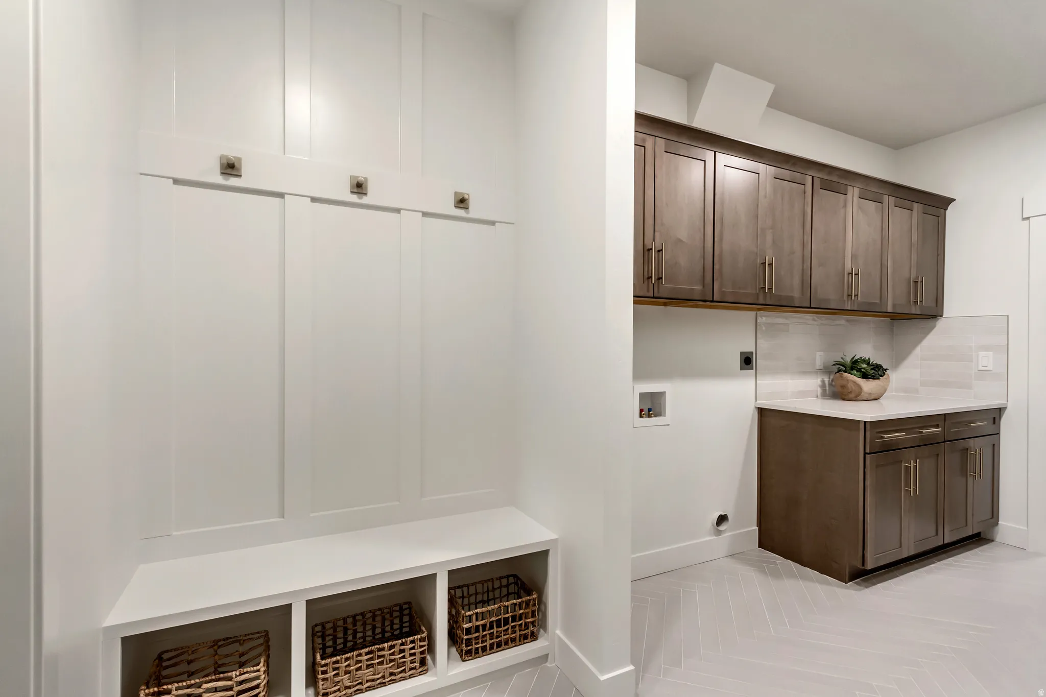 Built-in mudroom bench with cubby storage and coat hooks, complemented by an adjacent utility area featuring extensive cabinetry, countertop space, and a herringbone-patterned tile floor