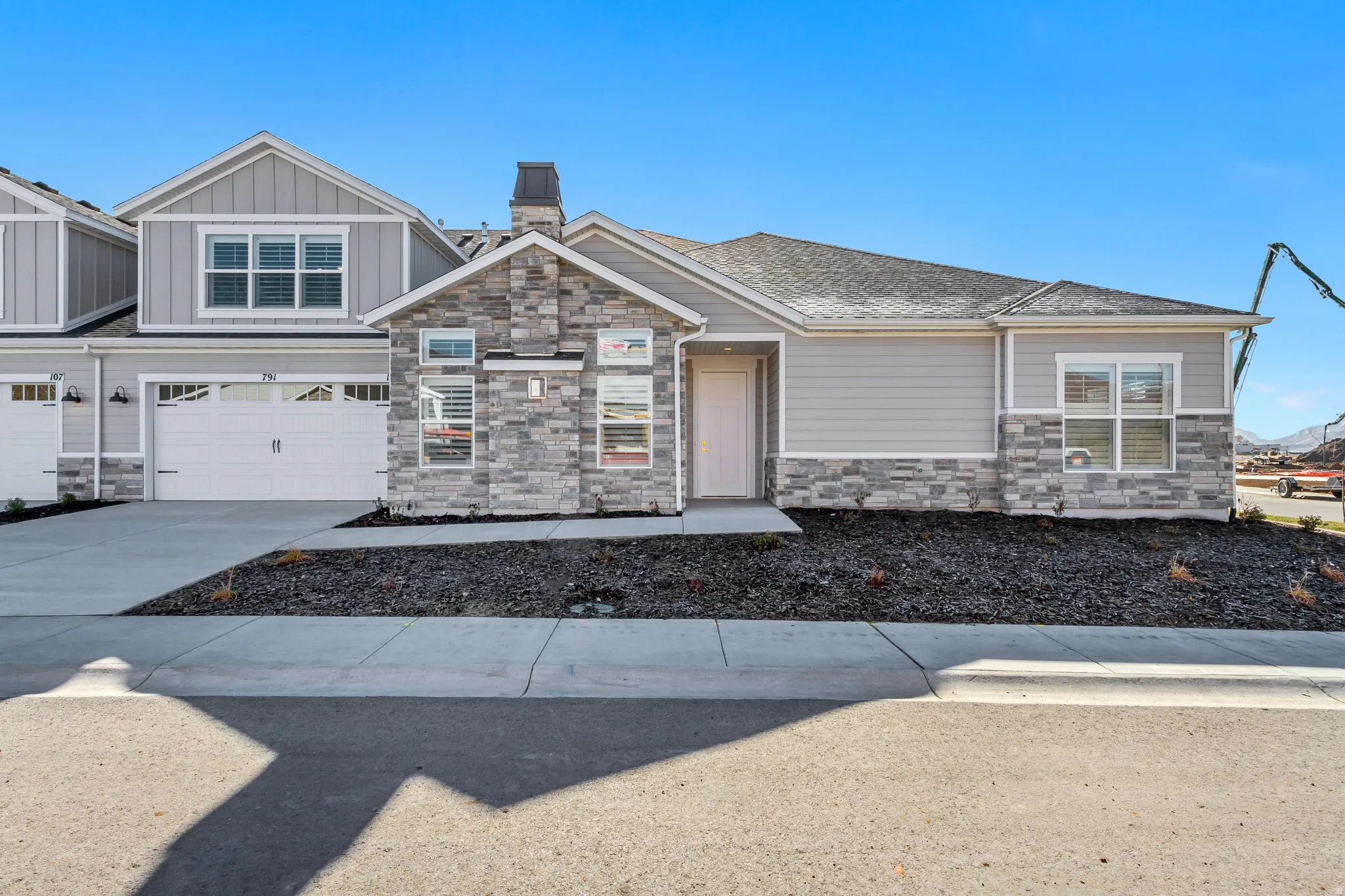 Exterior facade featuring light gray siding, stone veneer accents, white trim details, and a dark asphalt shingle roof