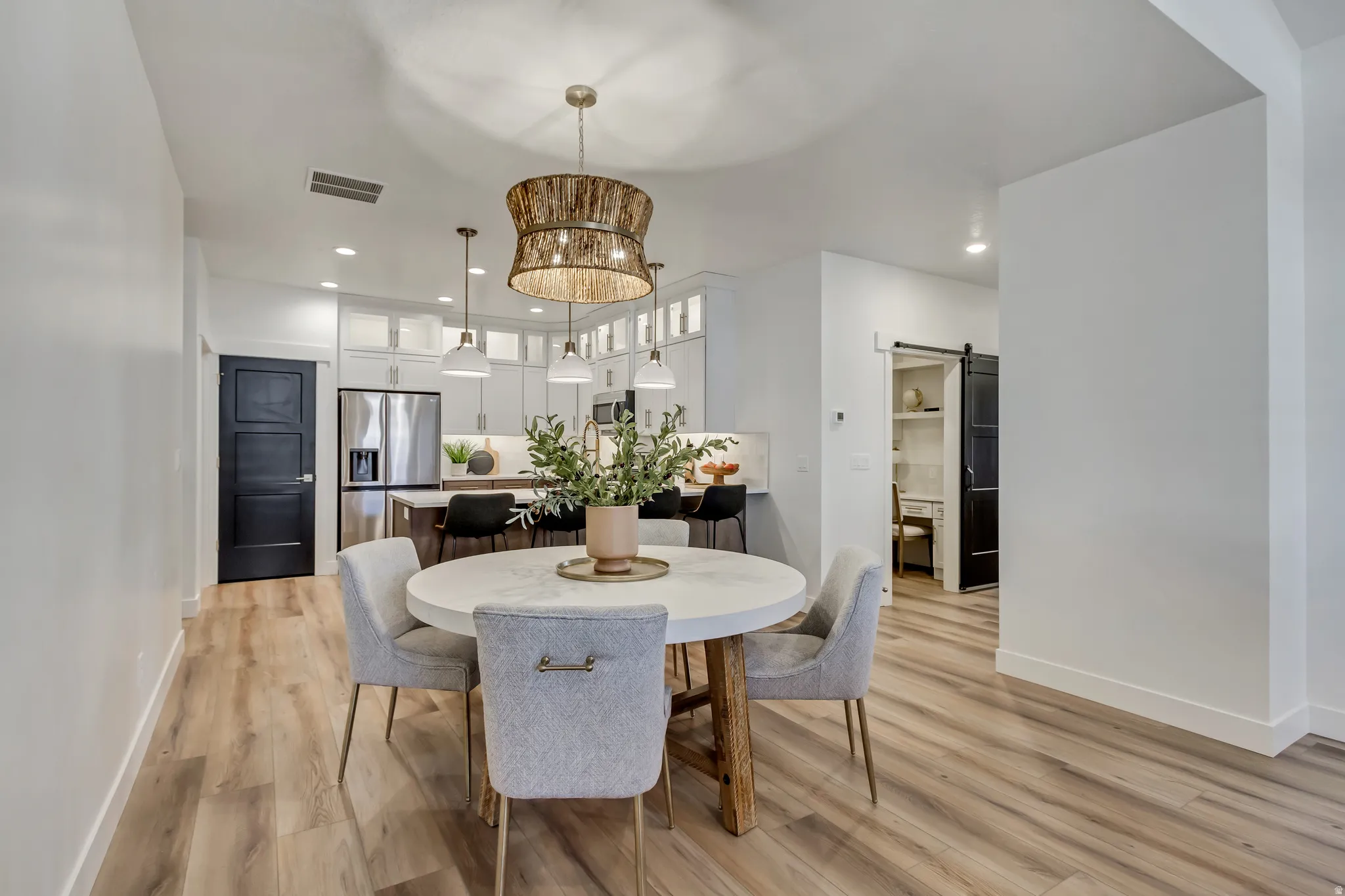 Open-concept dining area featuring light wood-finish flooring and a distinctive woven chandelier