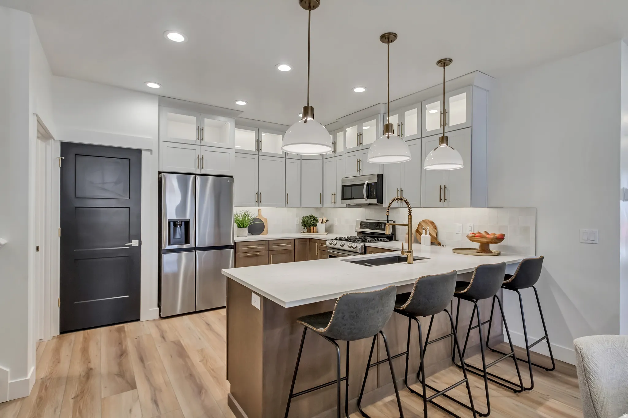 Contemporary kitchen featuring a large island with seating, stainless steel appliances, light wood-finish flooring, white cabinetry with glass inserts, and recessed lighting