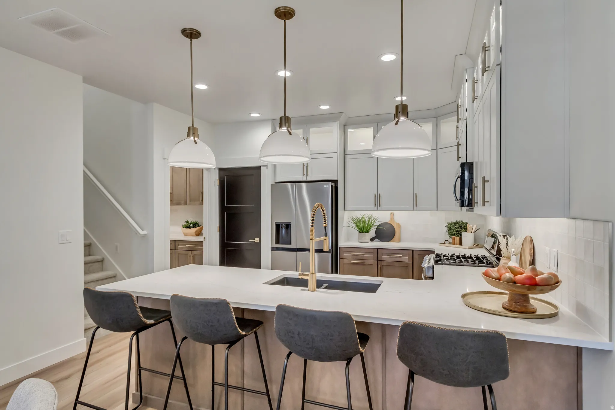 Modern kitchen featuring a large island with a composite countertop, an undermount sink with a brass-finish faucet, and three pendant lights