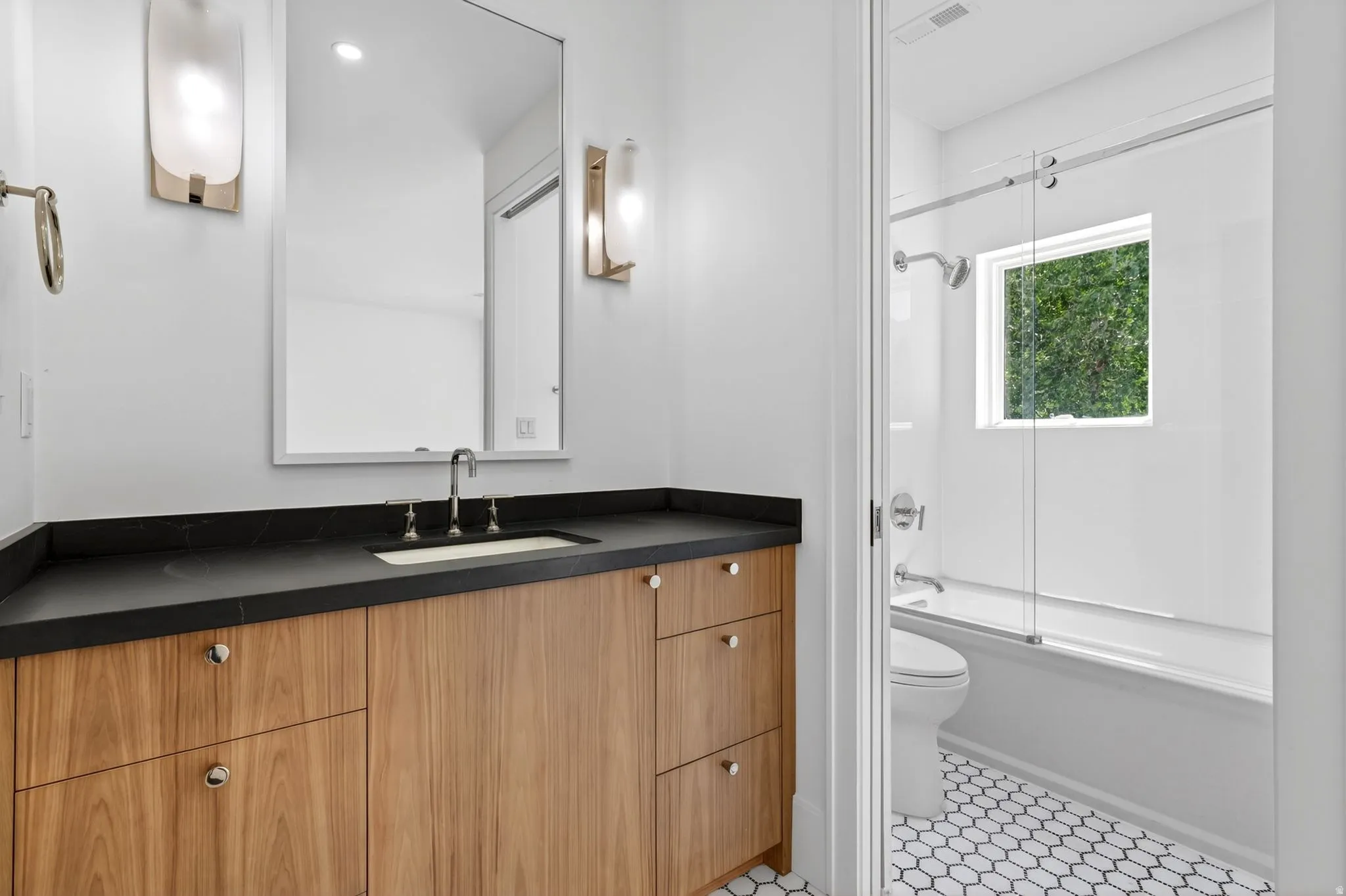 Bathroom featuring a wood-finish vanity with a dark countertop and integrated sink, framed mirror, and contemporary sconces