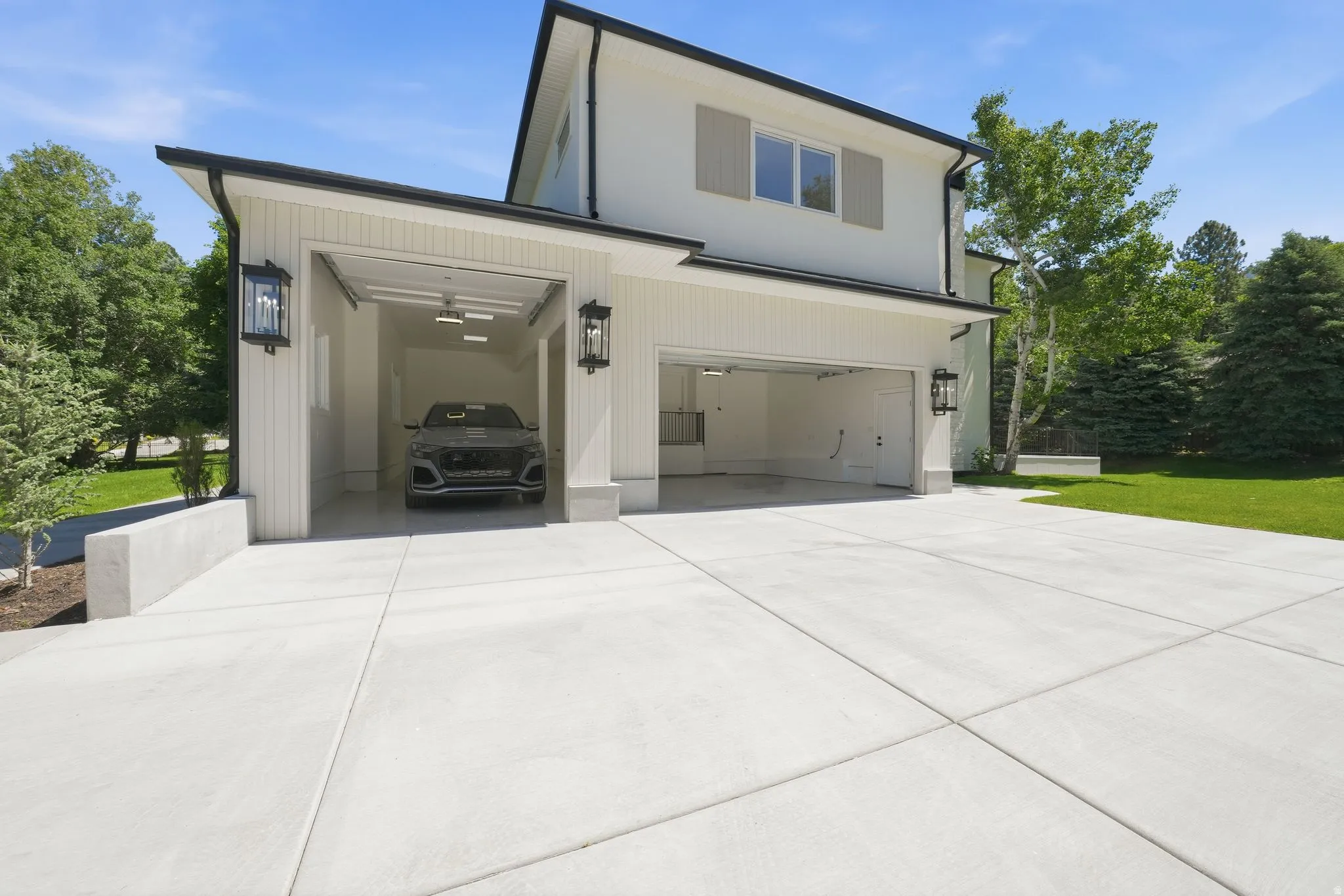 Contemporary home exterior featuring white vertical siding, black trim, and a spacious concrete driveway