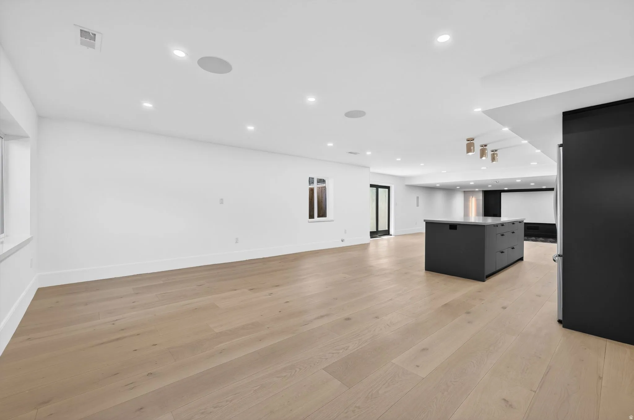 Open-concept living area featuring light wood-finish flooring, recessed lighting, and a contemporary dark-toned island with a light-toned countertop