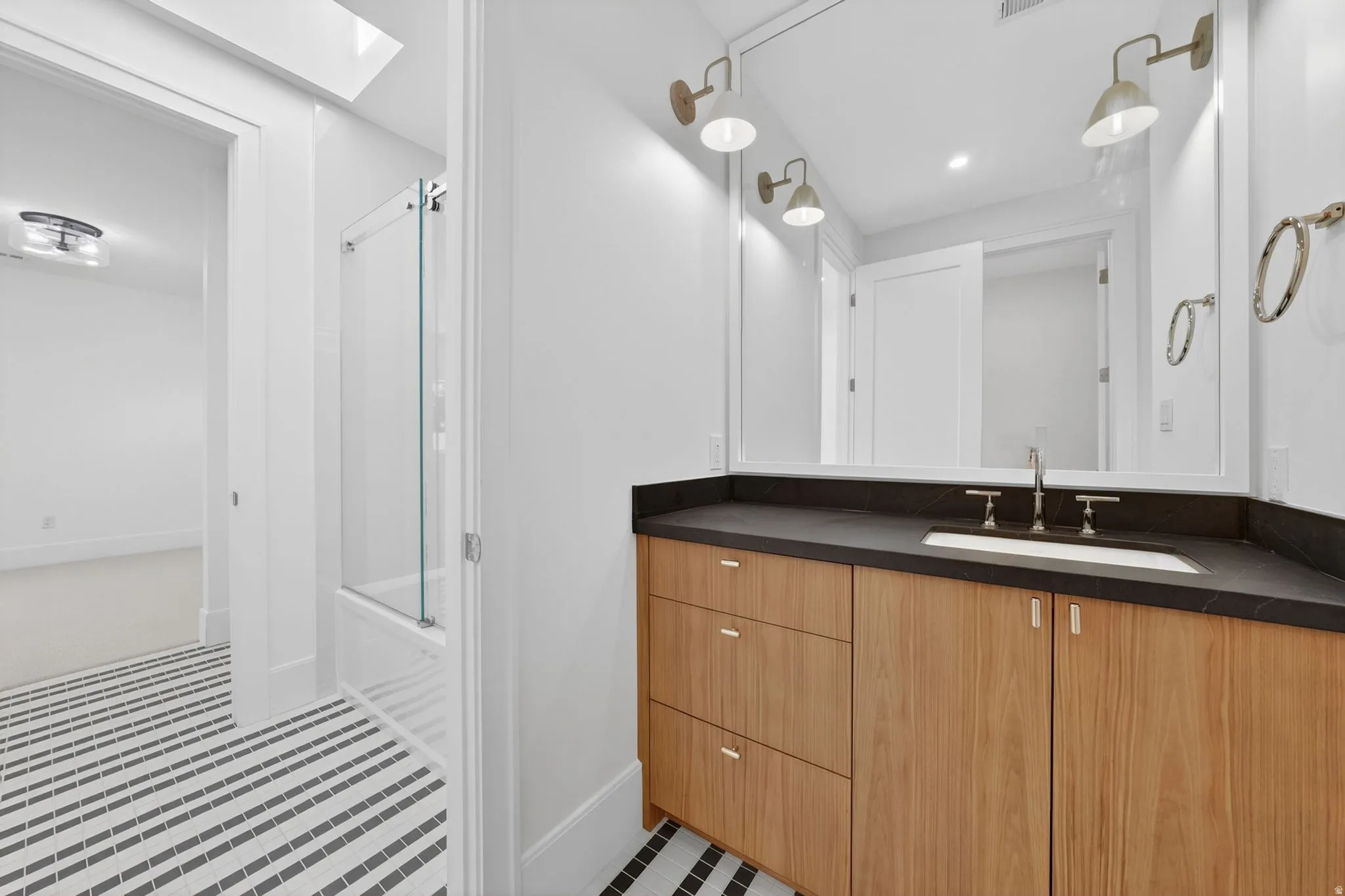 Bathroom featuring a wood-finish vanity with a dark countertop and integrated sink, under-mount lighting, and a large mirror