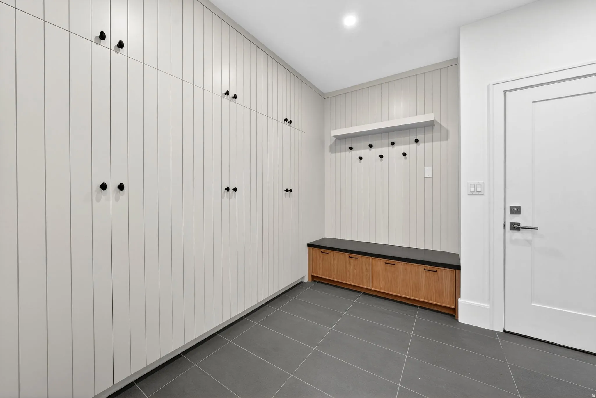Entryway mud room as you walk into the garage featuring plank-style storage cabinetry with matte black hardware, gray tile flooring, and a built-in wood-finish bench with a dark countertop