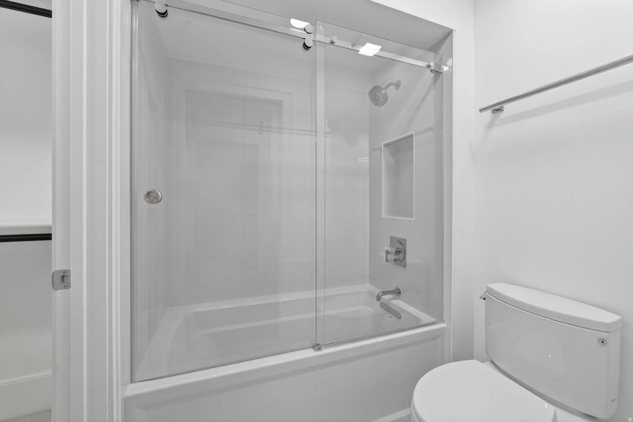 Bathtub with sliding glass enclosure featuring a built-in shower niche and chrome fixtures