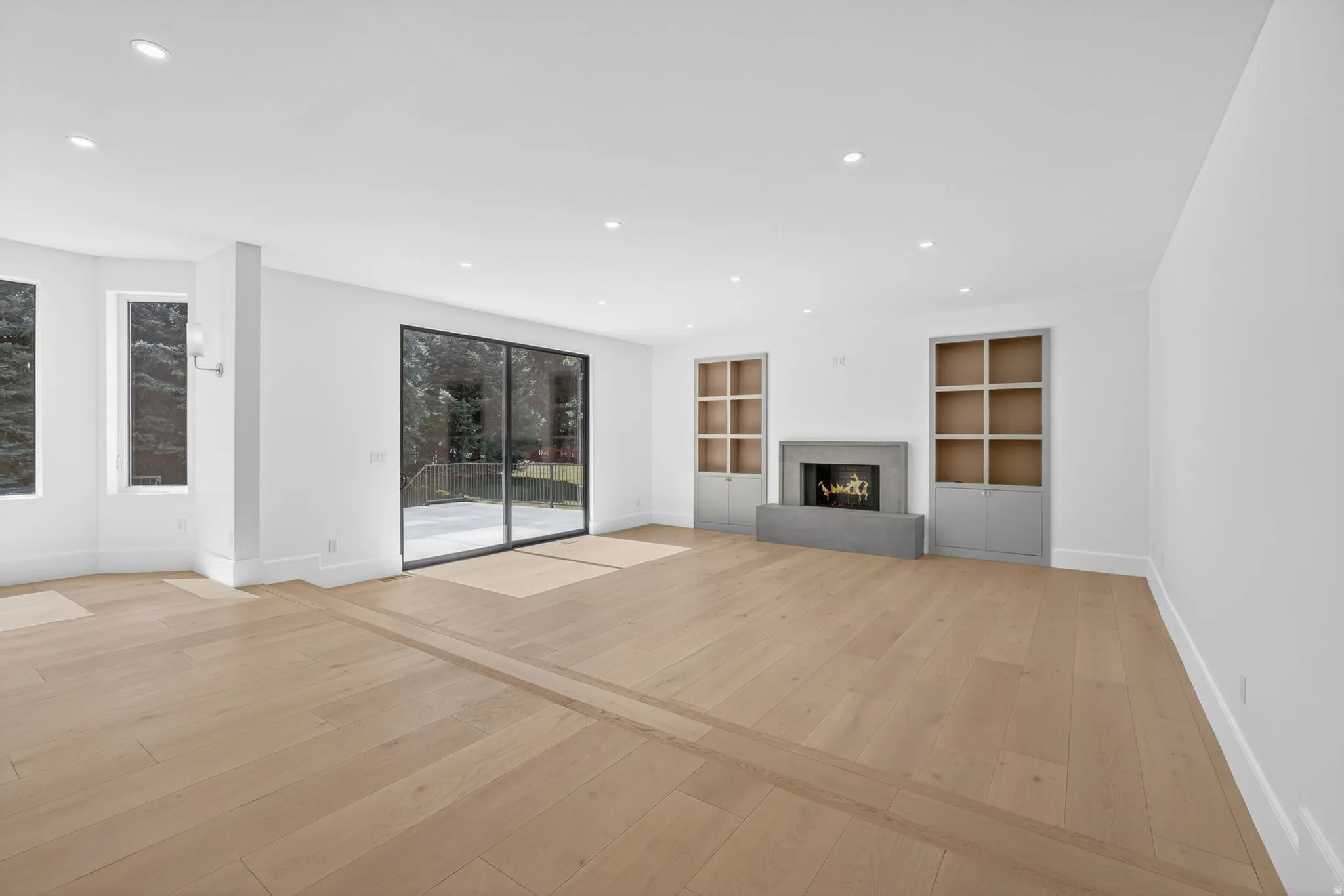 Spacious living room with light wood-finish flooring, recessed lighting, and a modern fireplace with a concrete surround with direct patio access in the backyard