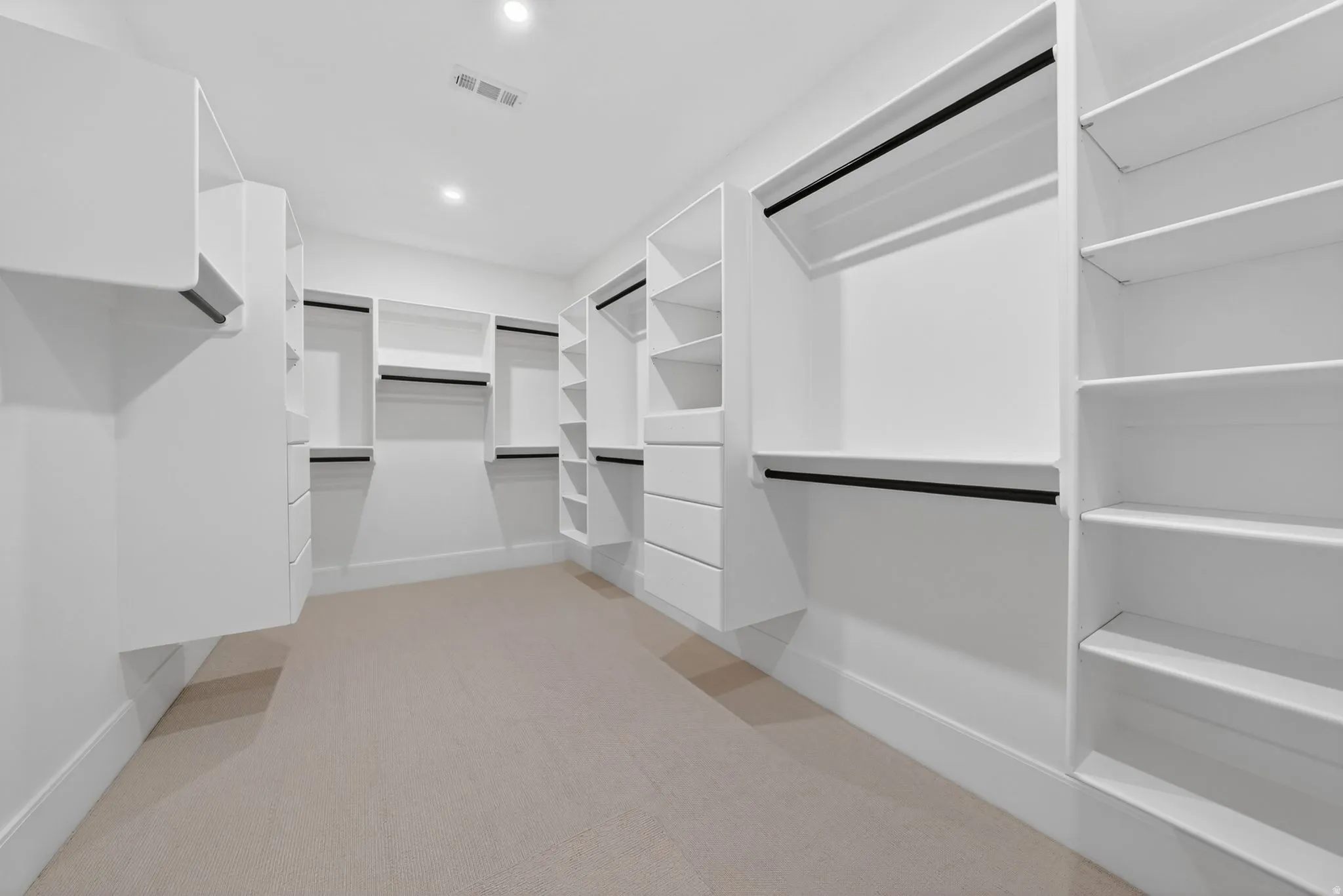 Spacious walk-in closet featuring built-in white cabinetry, multiple hanging rods, integrated shelving, and recessed ceiling lighting