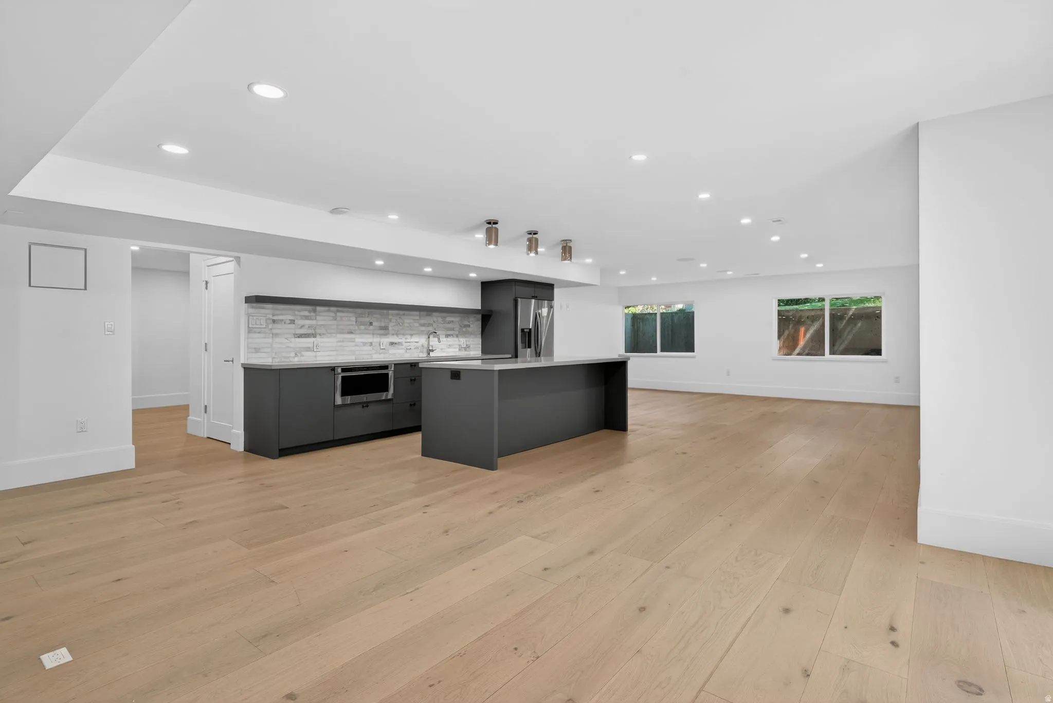 Downstairs kitchen with open-concept living area featuring light wood-finish flooring, recessed lighting, and a contemporary kitchen with walkout basement door