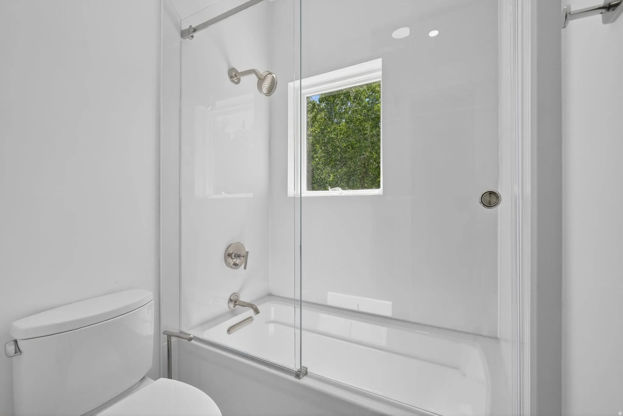 White bathroom featuring a shower-tub combination with clear glass enclosure and brushed nickel fixtures