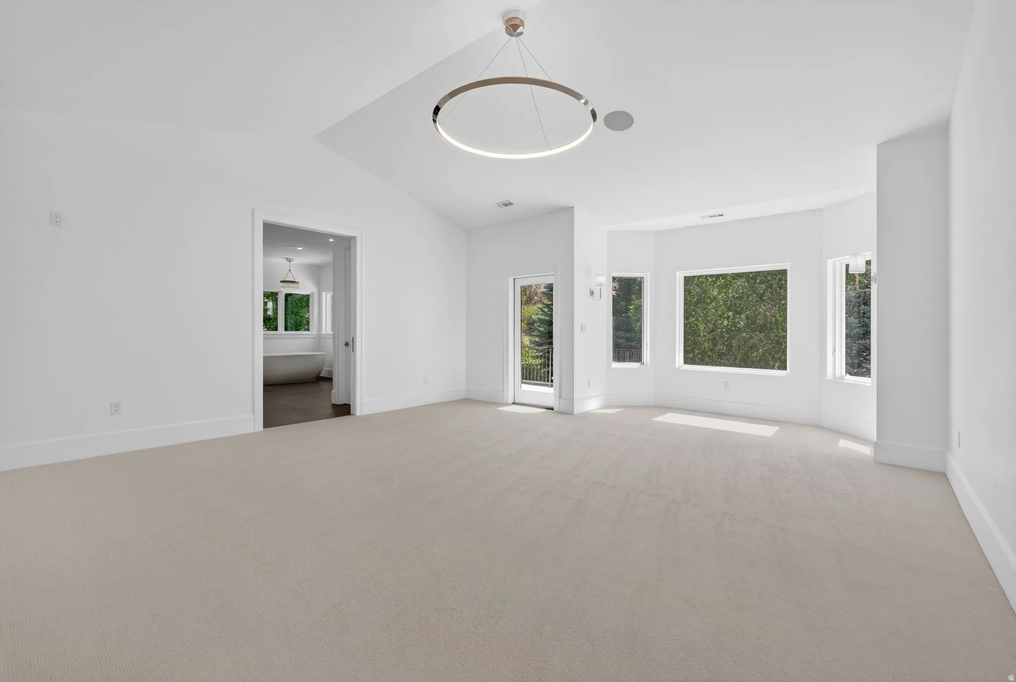 Spacious primary bedroom featuring vaulted ceilings, a contemporary circular light fixture, and light-toned carpeting