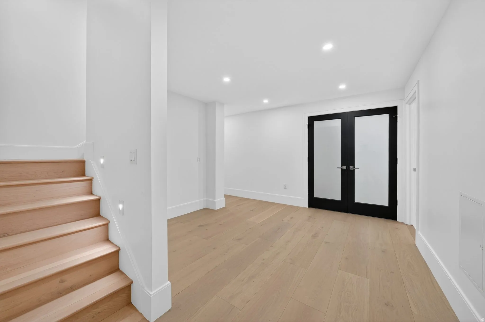 Spacious interior room featuring light wood-finish flooring, recessed ceiling lighting, and crisp white walls with thick baseboards