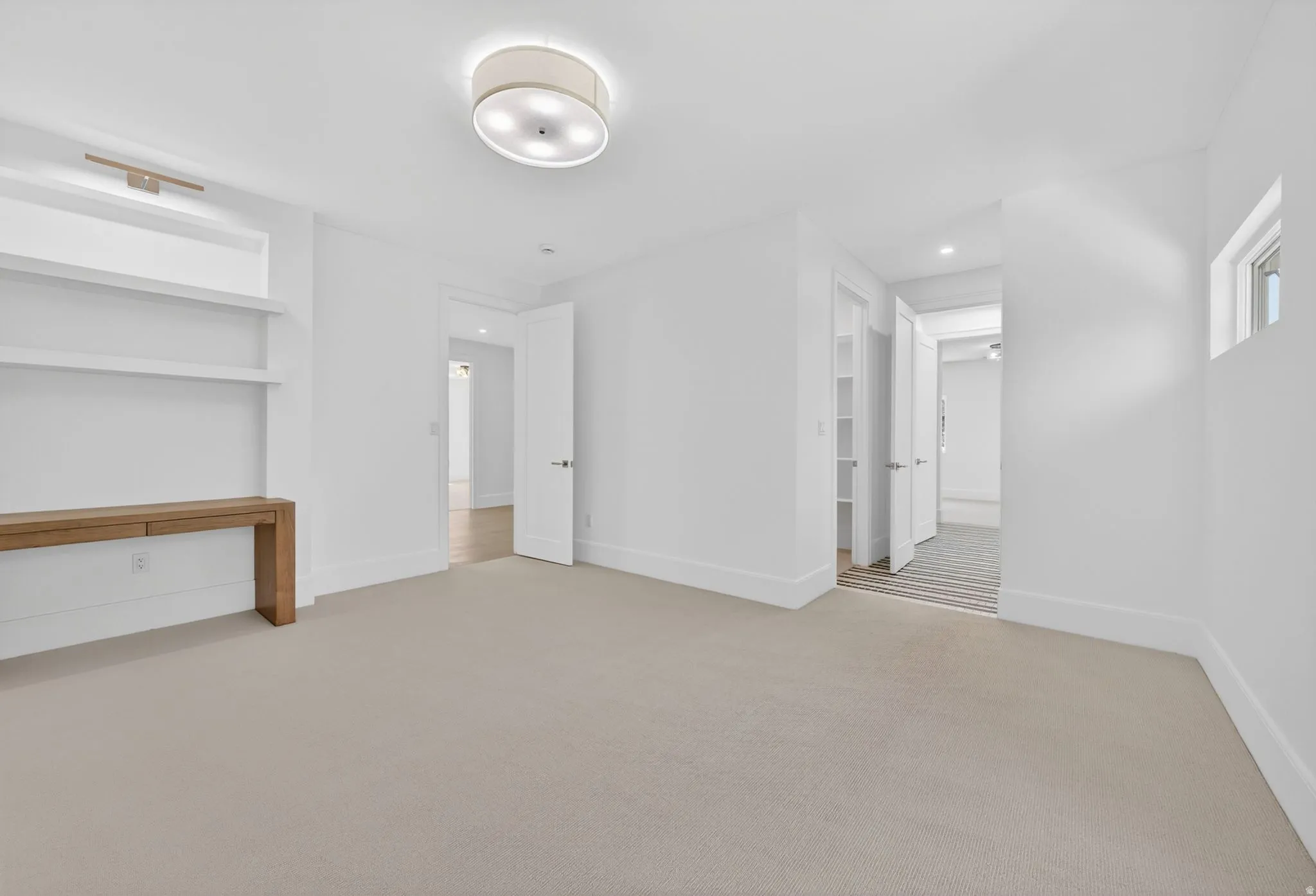 Carpeted room featuring a built-in wooden console with integrated shelving, a flush-mount ceiling light fixture, and white trim