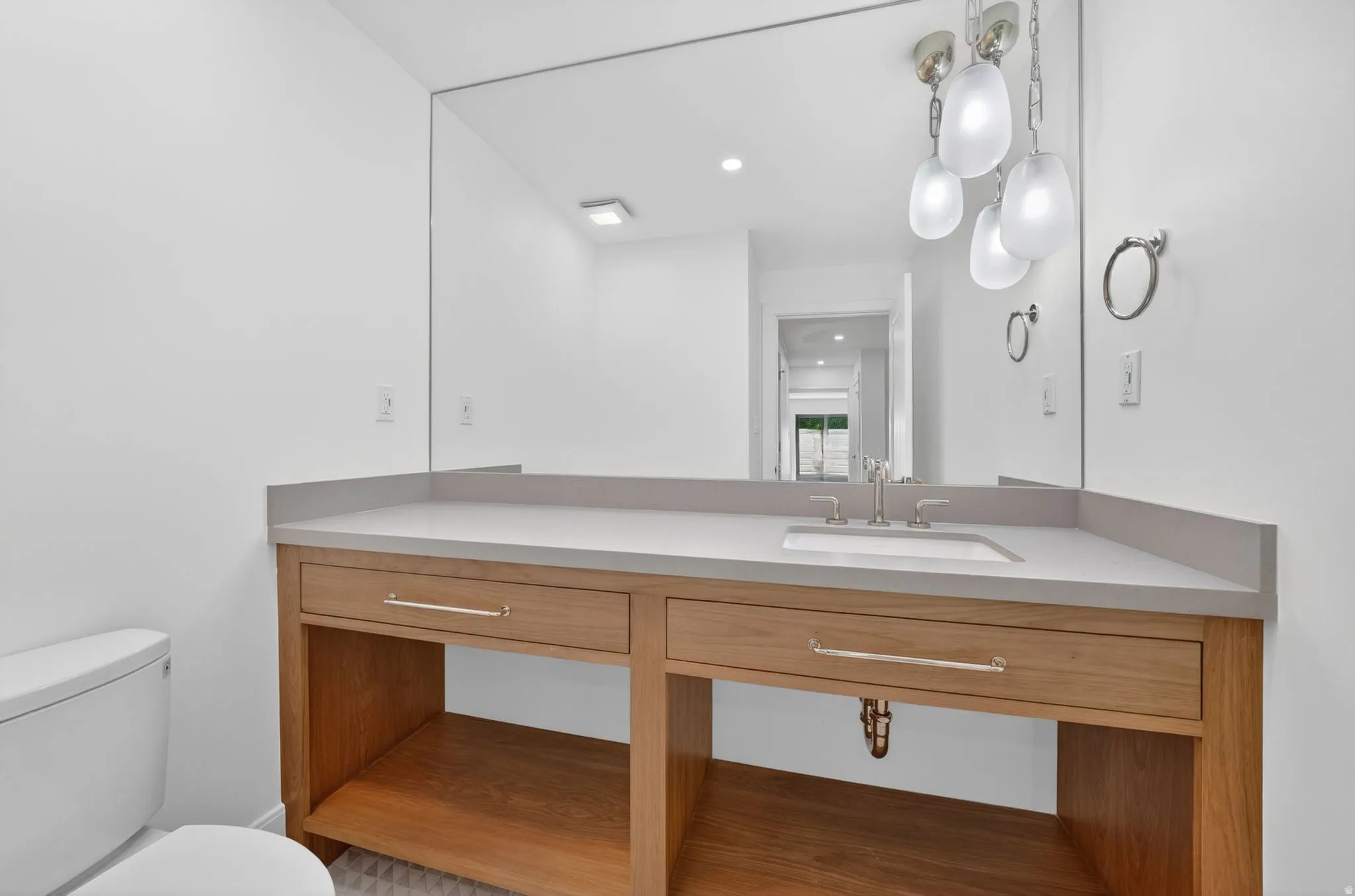 Bathroom vanity featuring a light wood-finish base with two drawers, a built-in open shelf, and a light gray countertop with an integrated sink