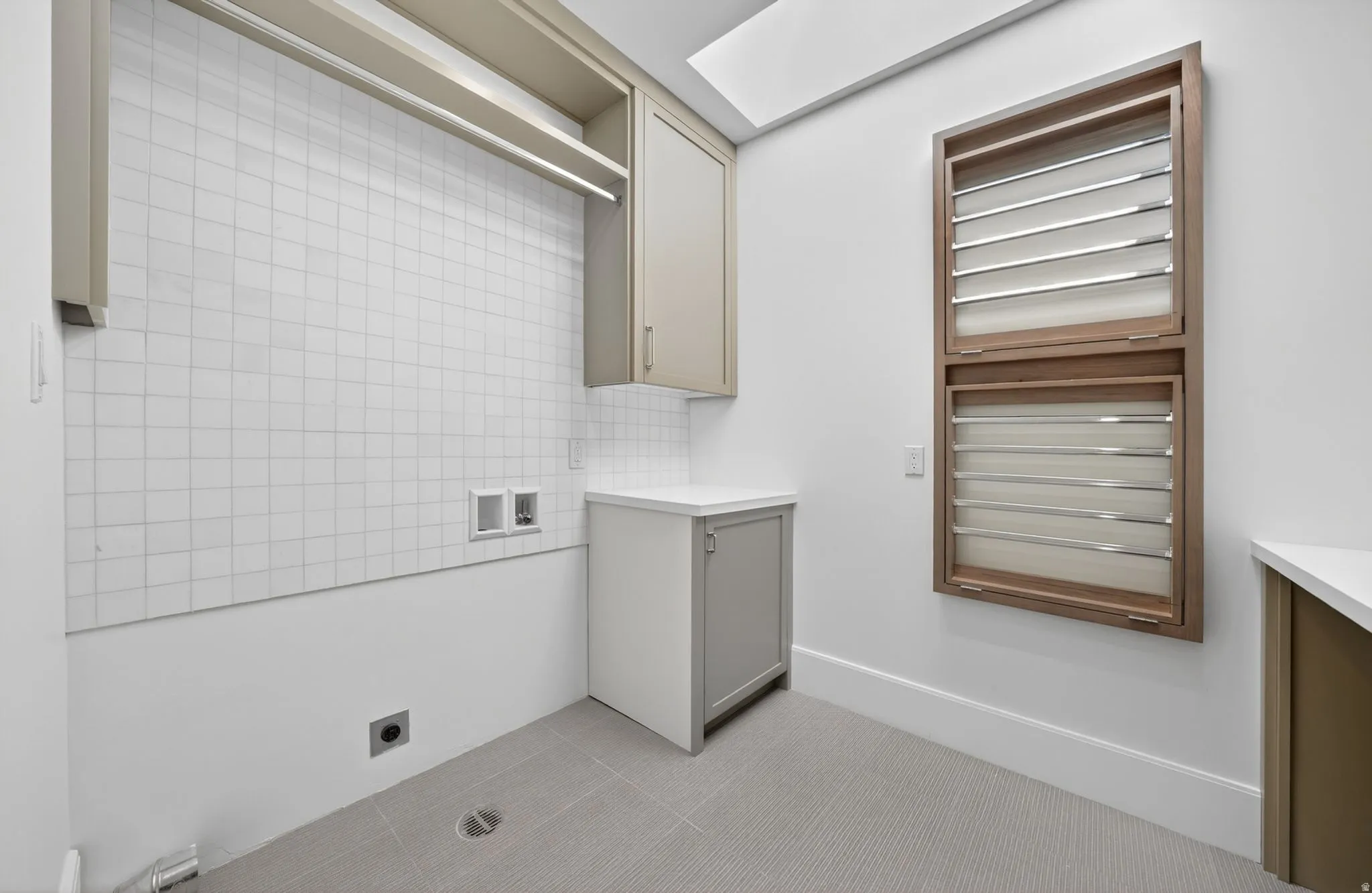 Laundry area with light-toned cabinetry, a built-in hanging rod, white square tile backsplash, and a wall-mounted drying rack