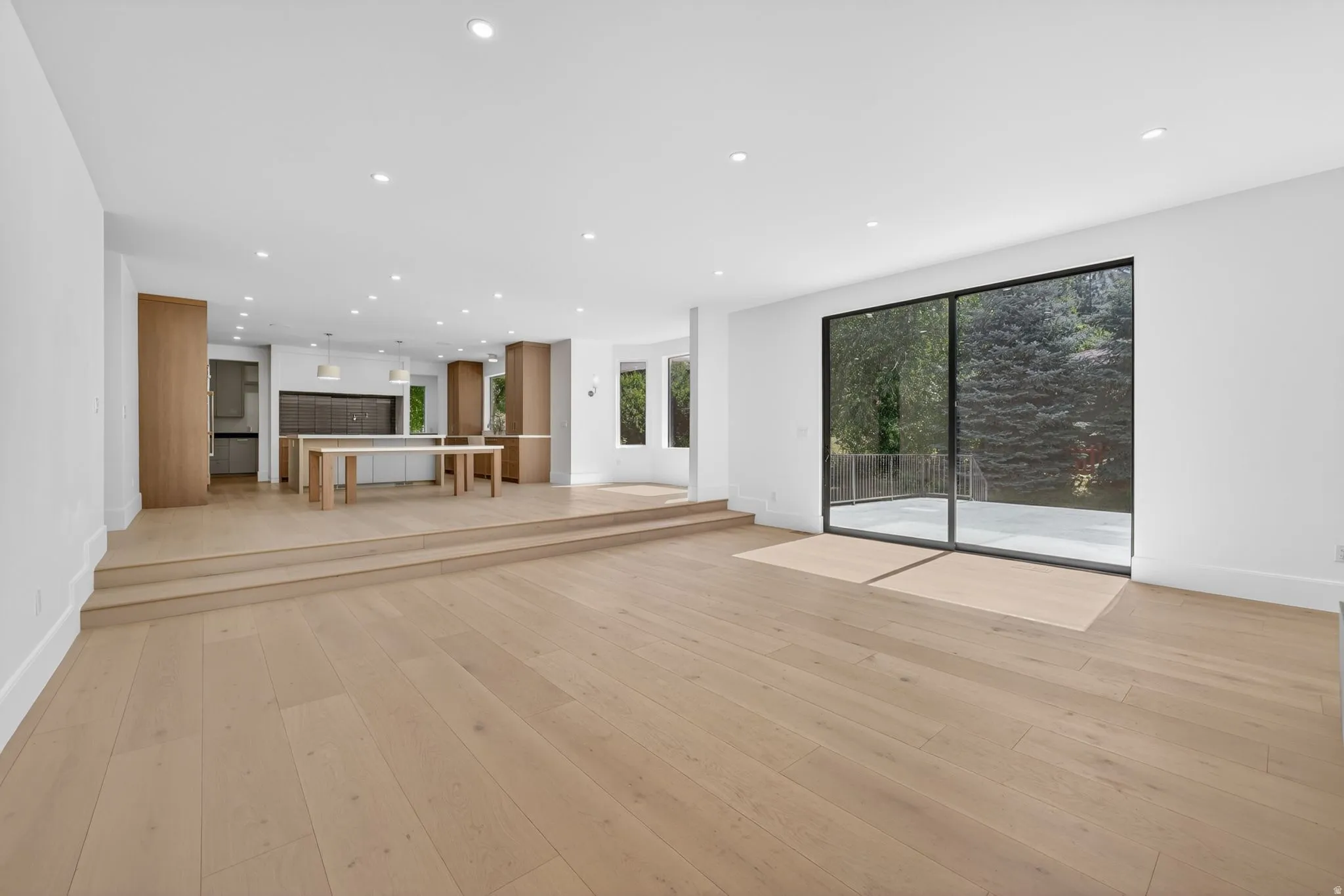 Open-concept living space featuring wood-finish flooring, recessed lighting, and a multi-level design with direct patio access and sliding screen doors