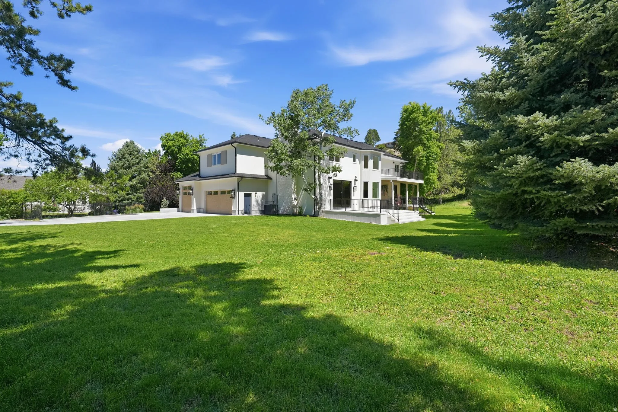 Expansive green lawn bordering a two-story stucco residence with a black roof, multiple balconies with dark railings, and a two-car garage with wood-finish doors