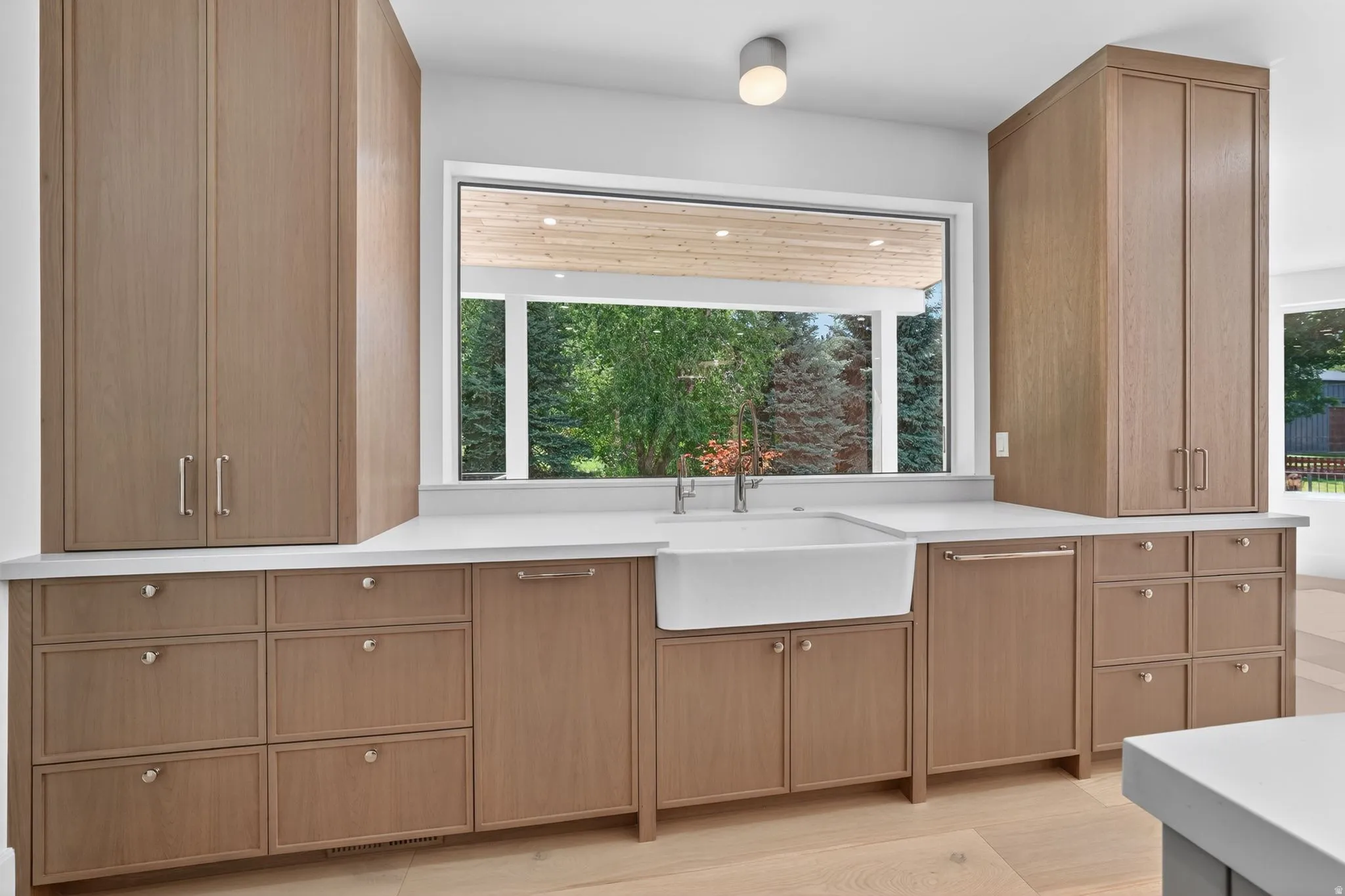 Kitchen featuring a large farm sink with a dual-handle faucet, white countertops, and extensive wood-finish cabinetry