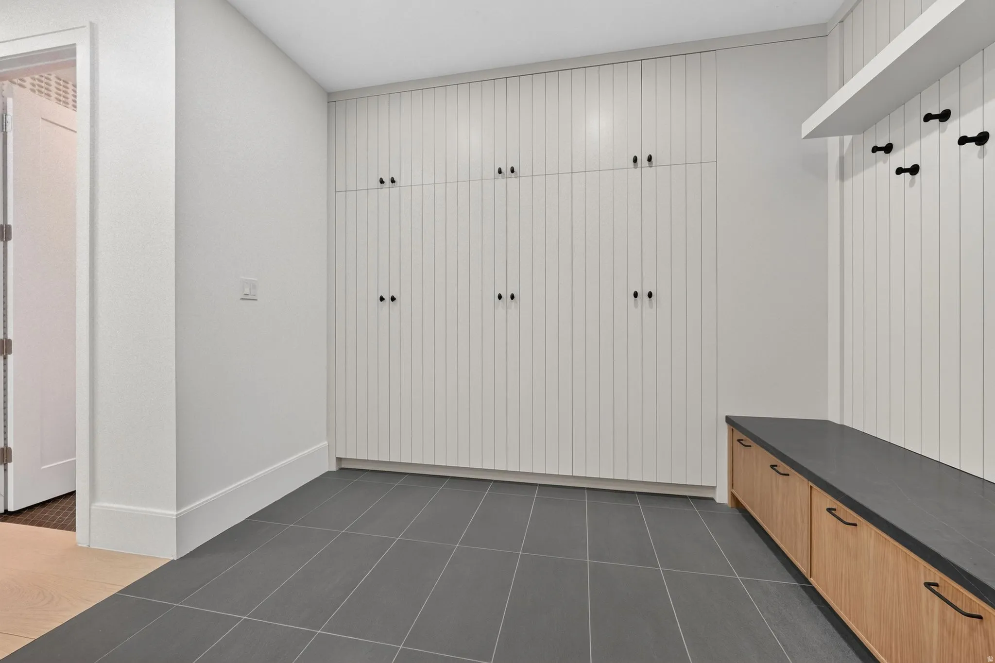 Entryway featuring extensive built-in storage cabinetry, dark gray floor tiling, a wood-finish bench with integrated storage drawers, a floating shelf, and wall-mounted hooks