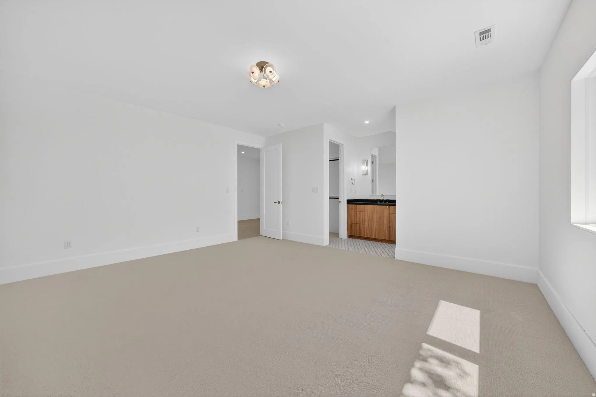 Spacious room featuring neutral carpeting, white baseboards, and a modern flush-mount ceiling light