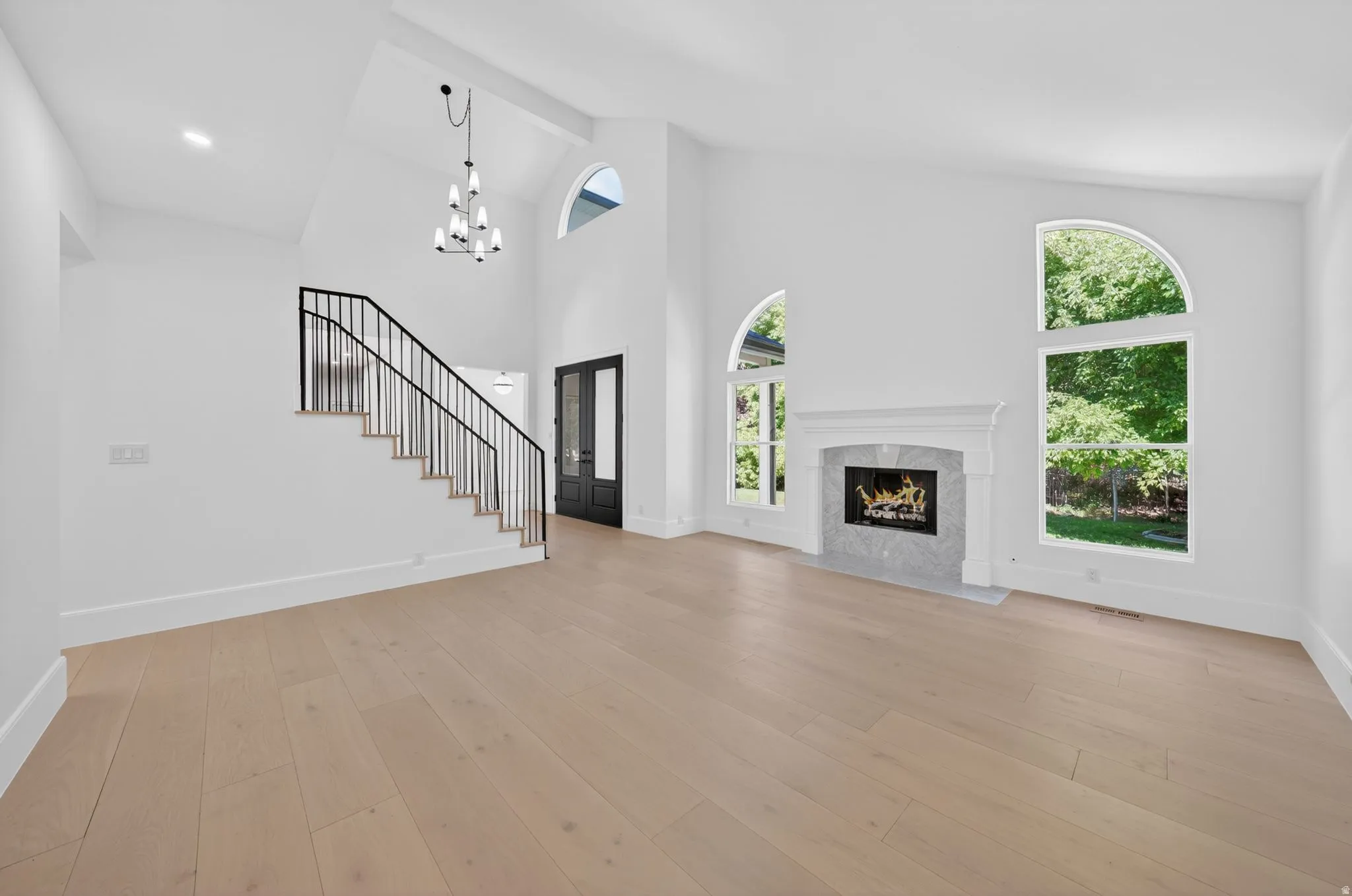 Spacious living area featuring high vaulted ceilings, light wood-finish flooring, a traditional fireplace with a light stone surround, and arched windows