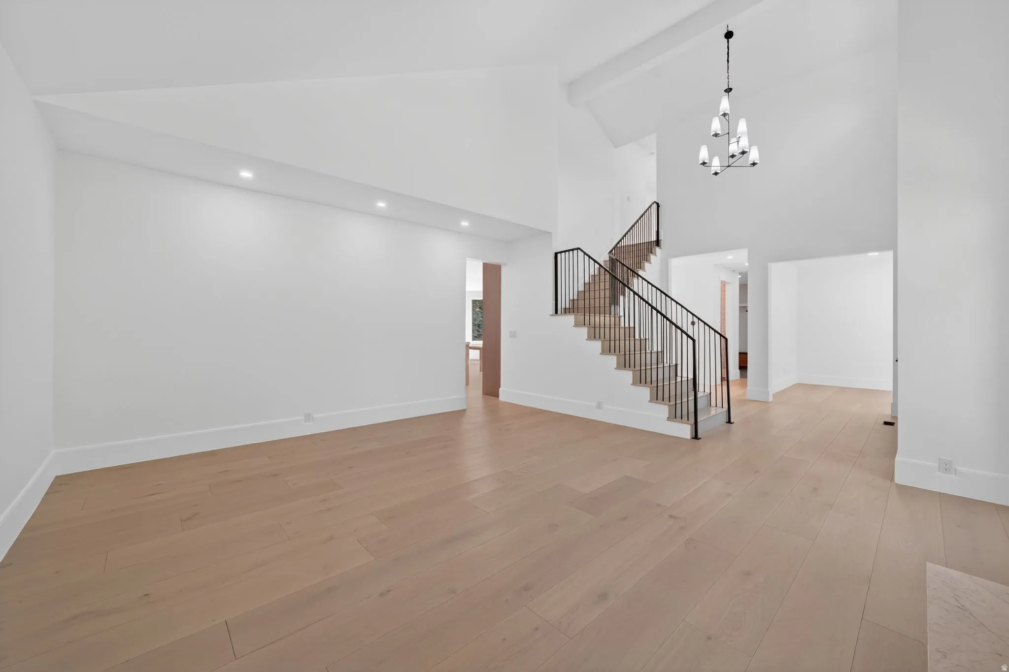 Expansive living area with vaulted ceilings, light wood-finish flooring, and recessed lighting