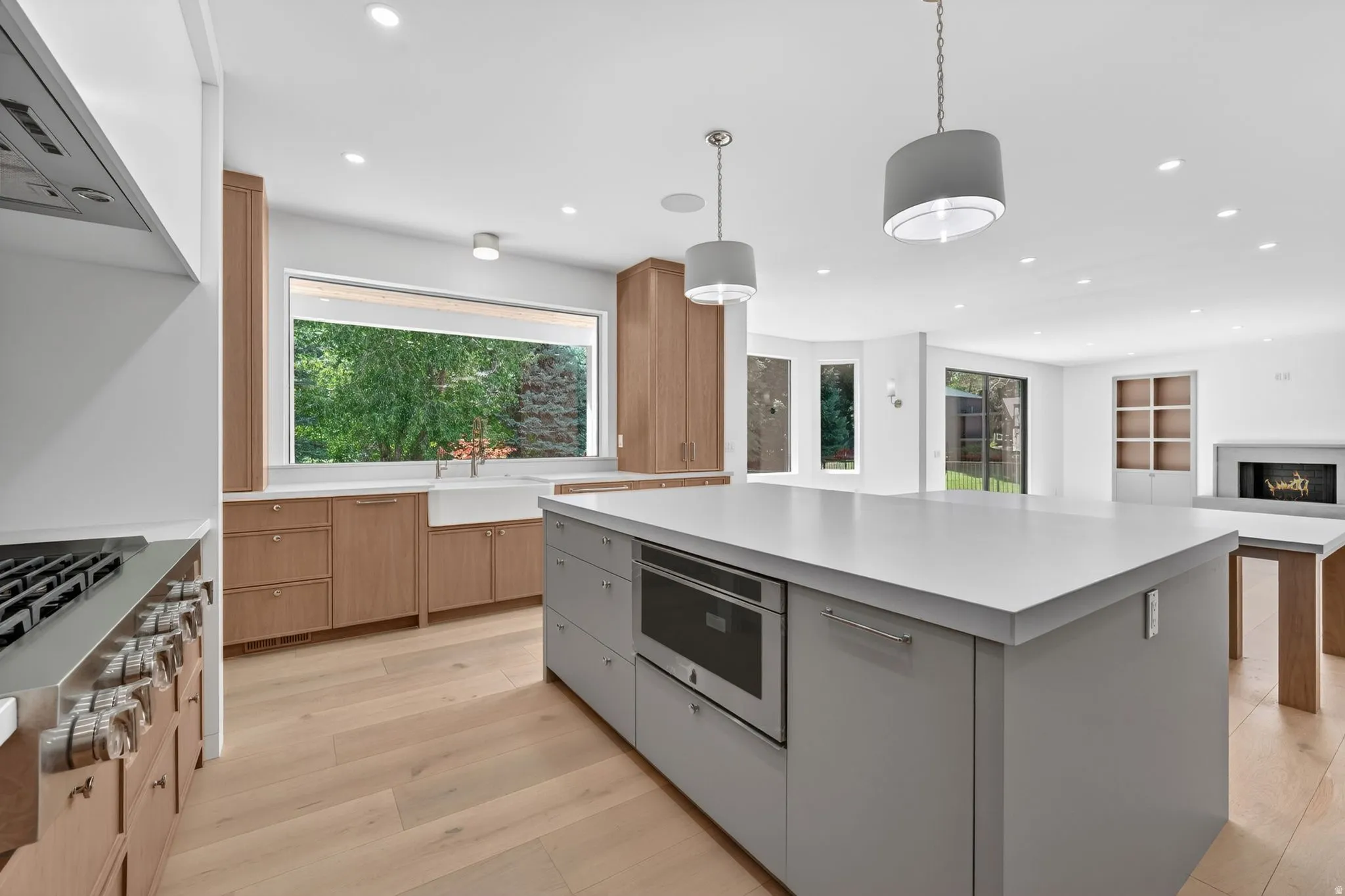 Contemporary kitchen featuring a large center island with integrated microwave, light wood-finish cabinetry, a farmhouse-style sink under a wide window, and recessed lighting