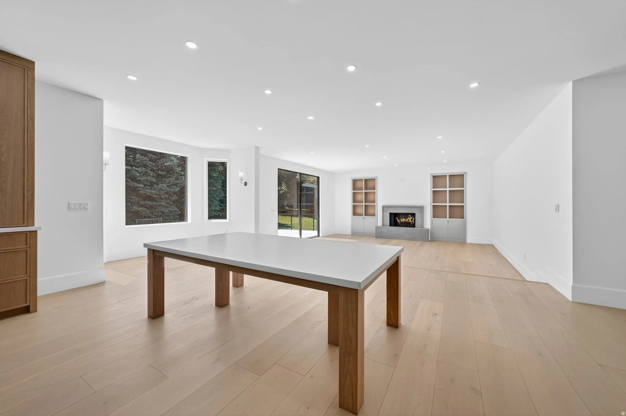 Open-concept interior featuring light wood-finish flooring, recessed lighting, built in table and a modern fireplace with built-in shelving