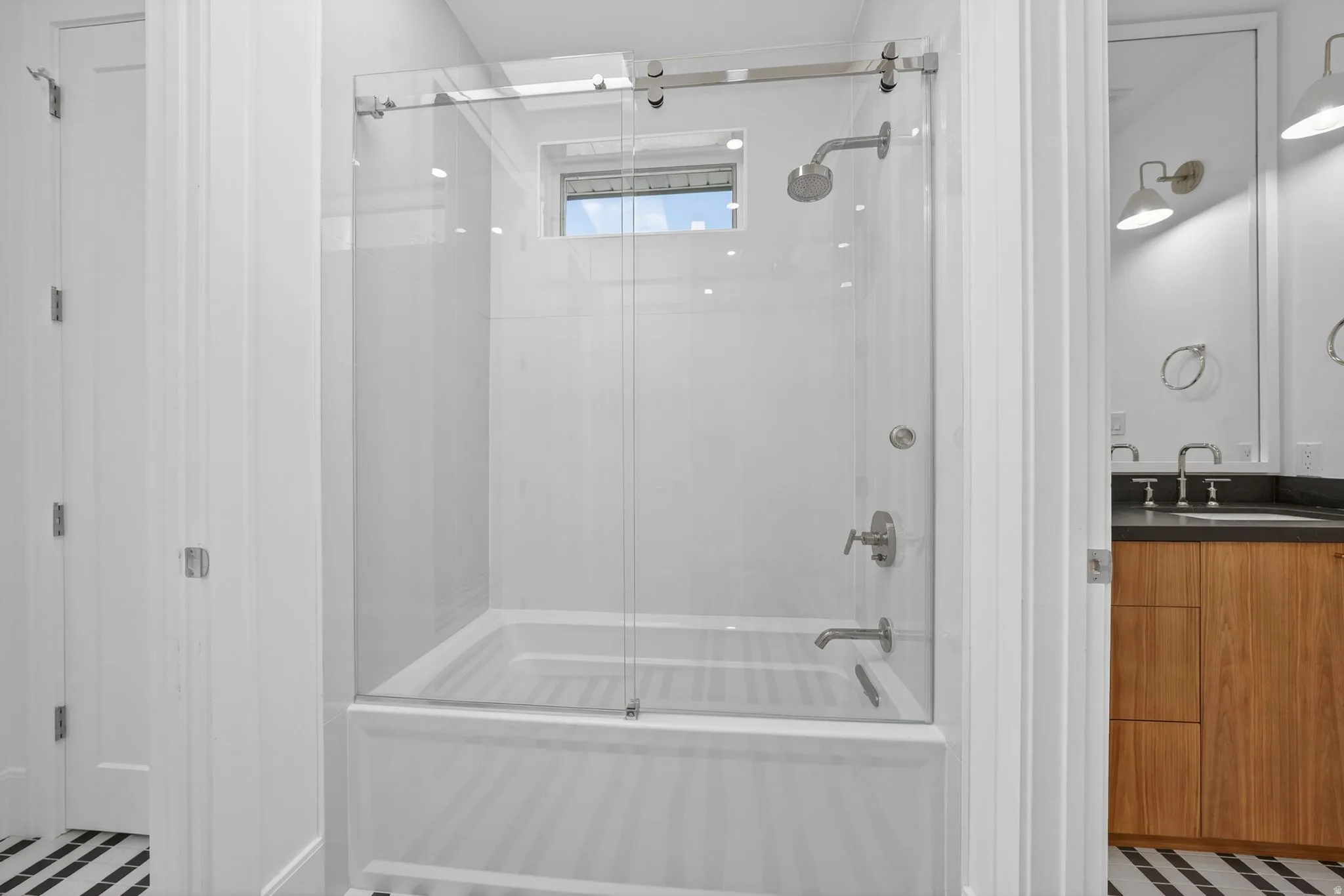 Tub and shower combination featuring a clear glass enclosure, a rain showerhead, and chrome fixtures