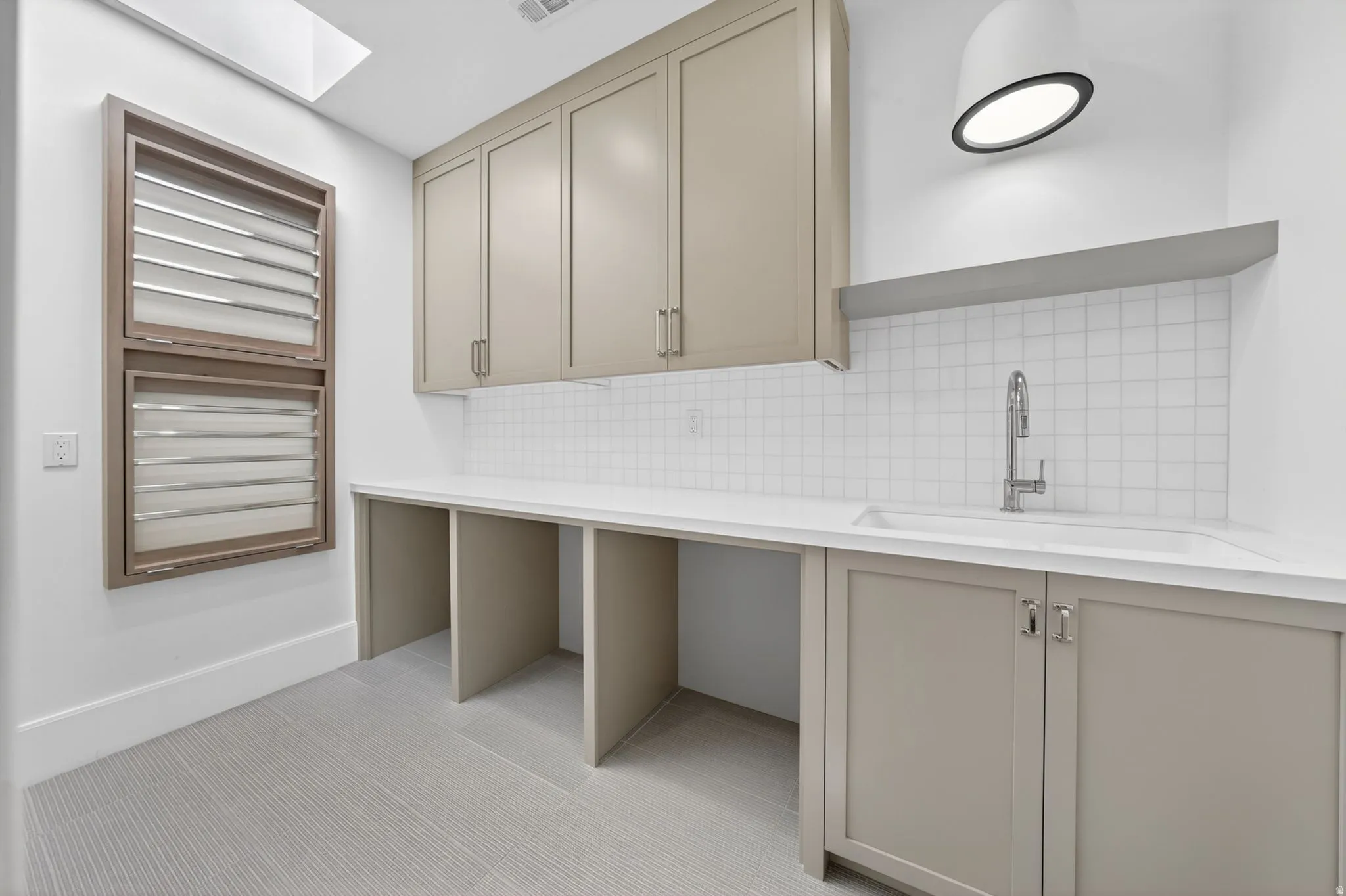 Secondary laundry room featuring light-toned cabinetry, white subway tile backsplash, a built-in sink with a gooseneck faucet, and a large countertop with integrated workspace areas