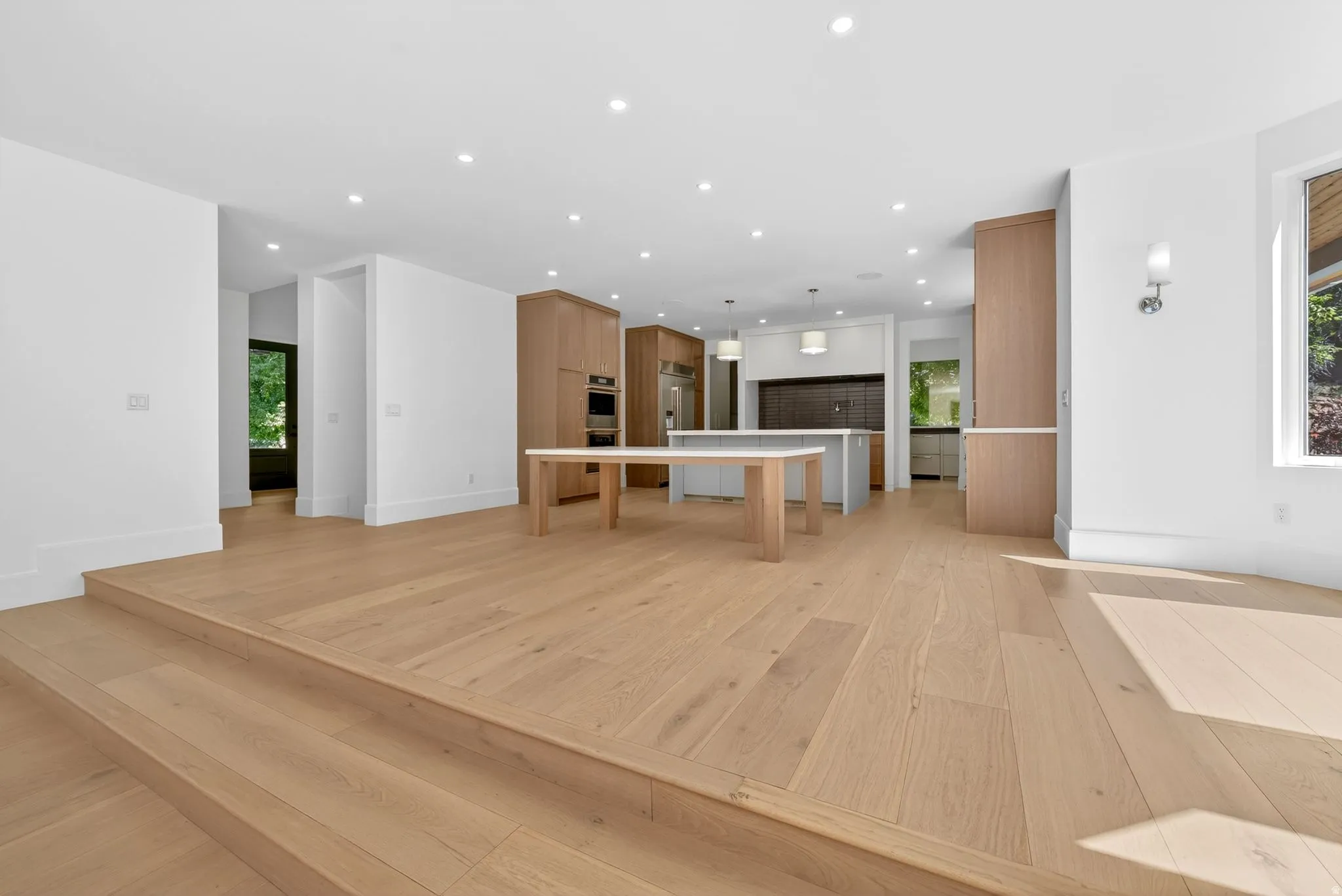Open-concept living area with light wood-finish flooring and recessed lighting