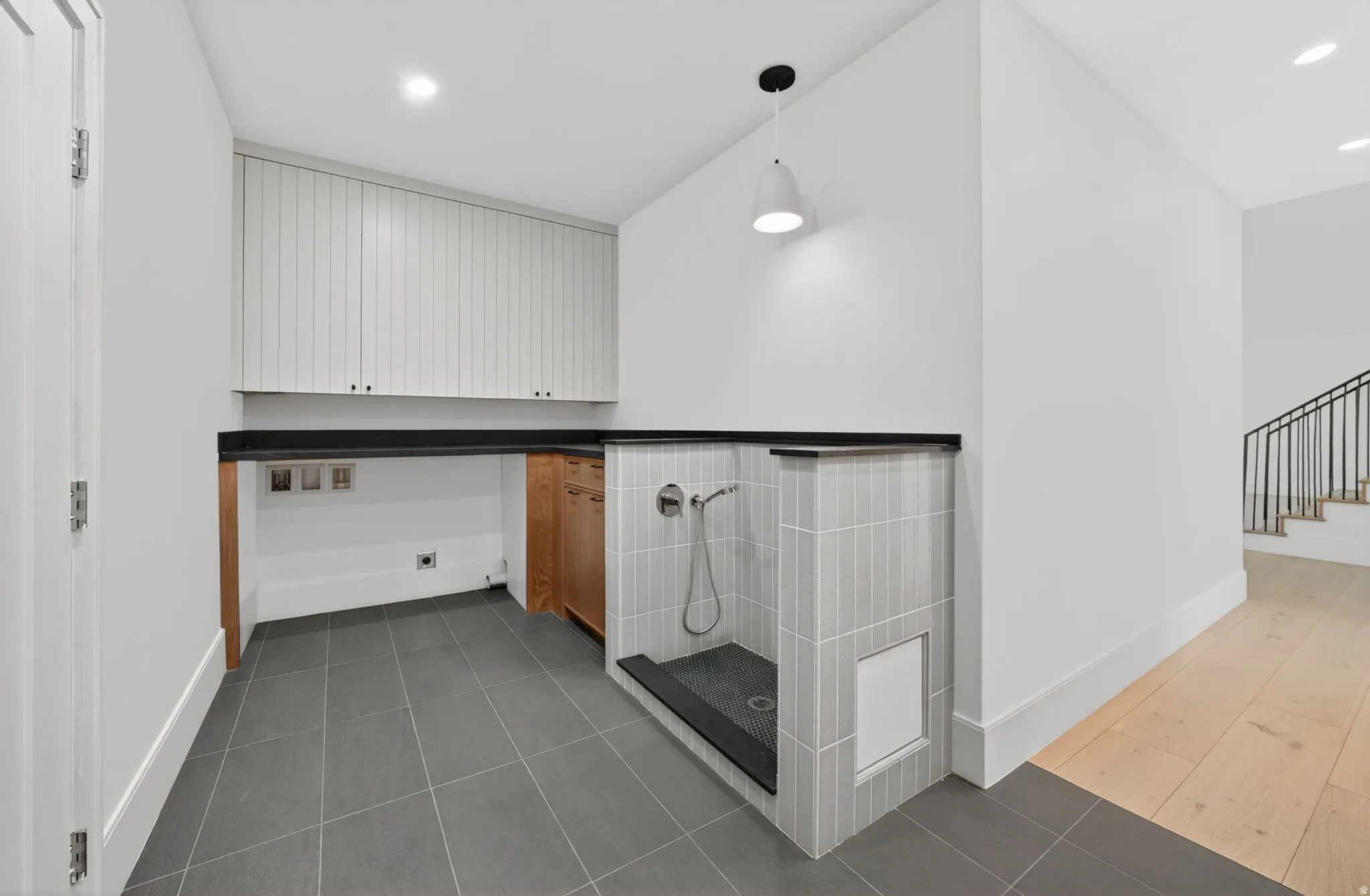 Dedicated dog wash utility space featuring tile flooring, beadboard upper cabinetry, a dark countertop, a built-in pet wash station with vertical subway tile, and a wall-mounted shower head
