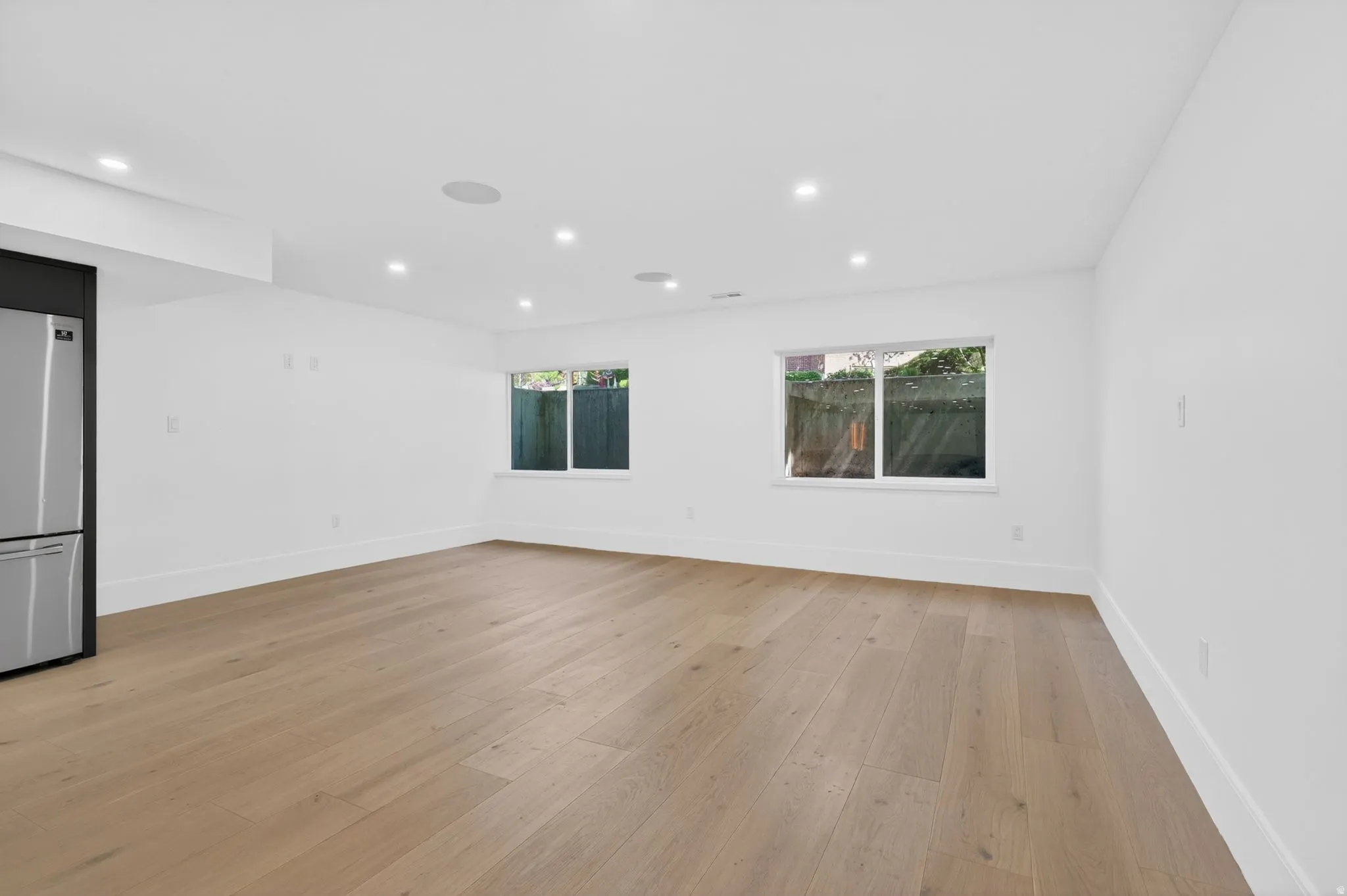 Spacious room featuring wood-finish flooring, recessed lighting, and two windows